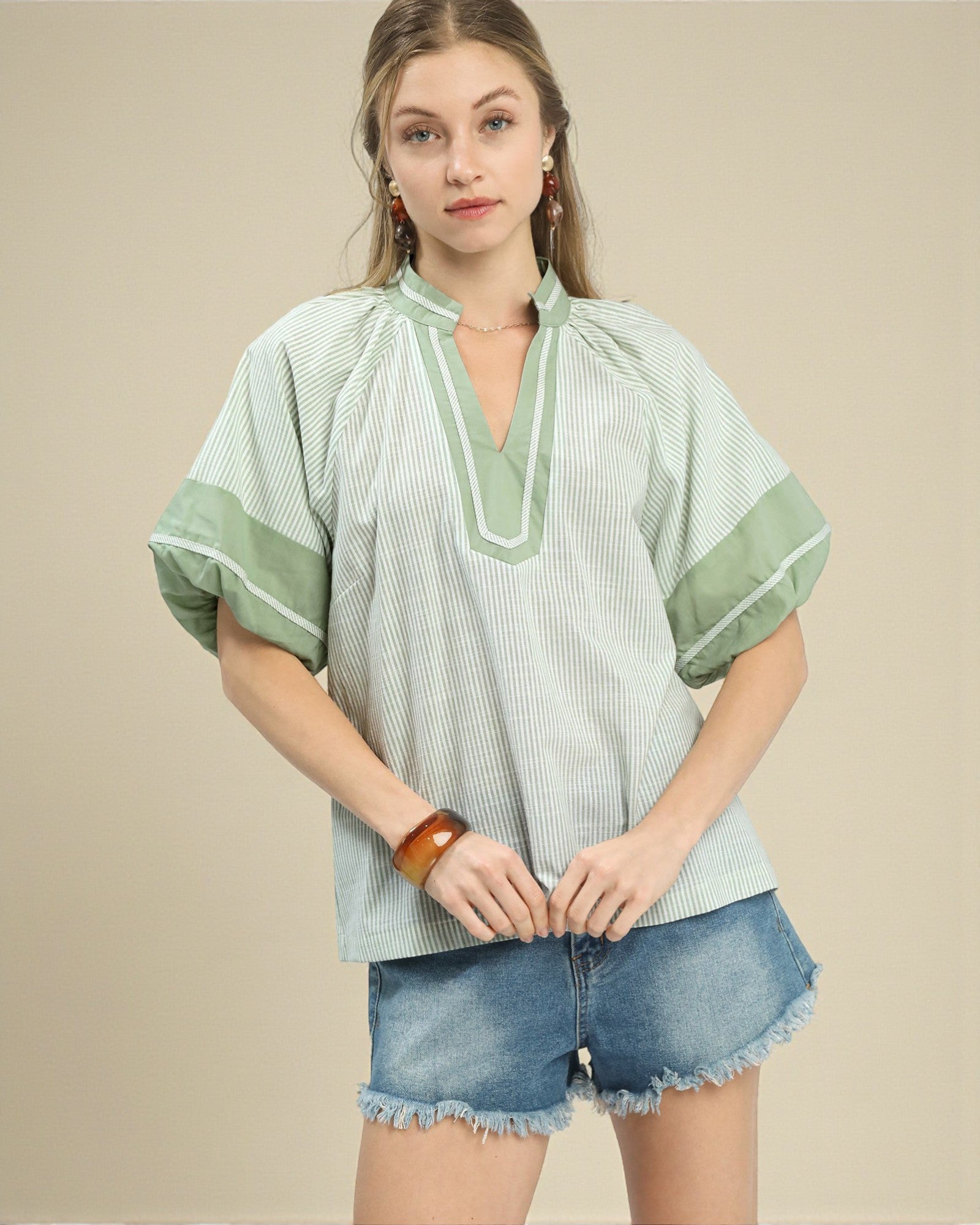 Woman wearing a green and white striped shirt with denim shorts on a beige background