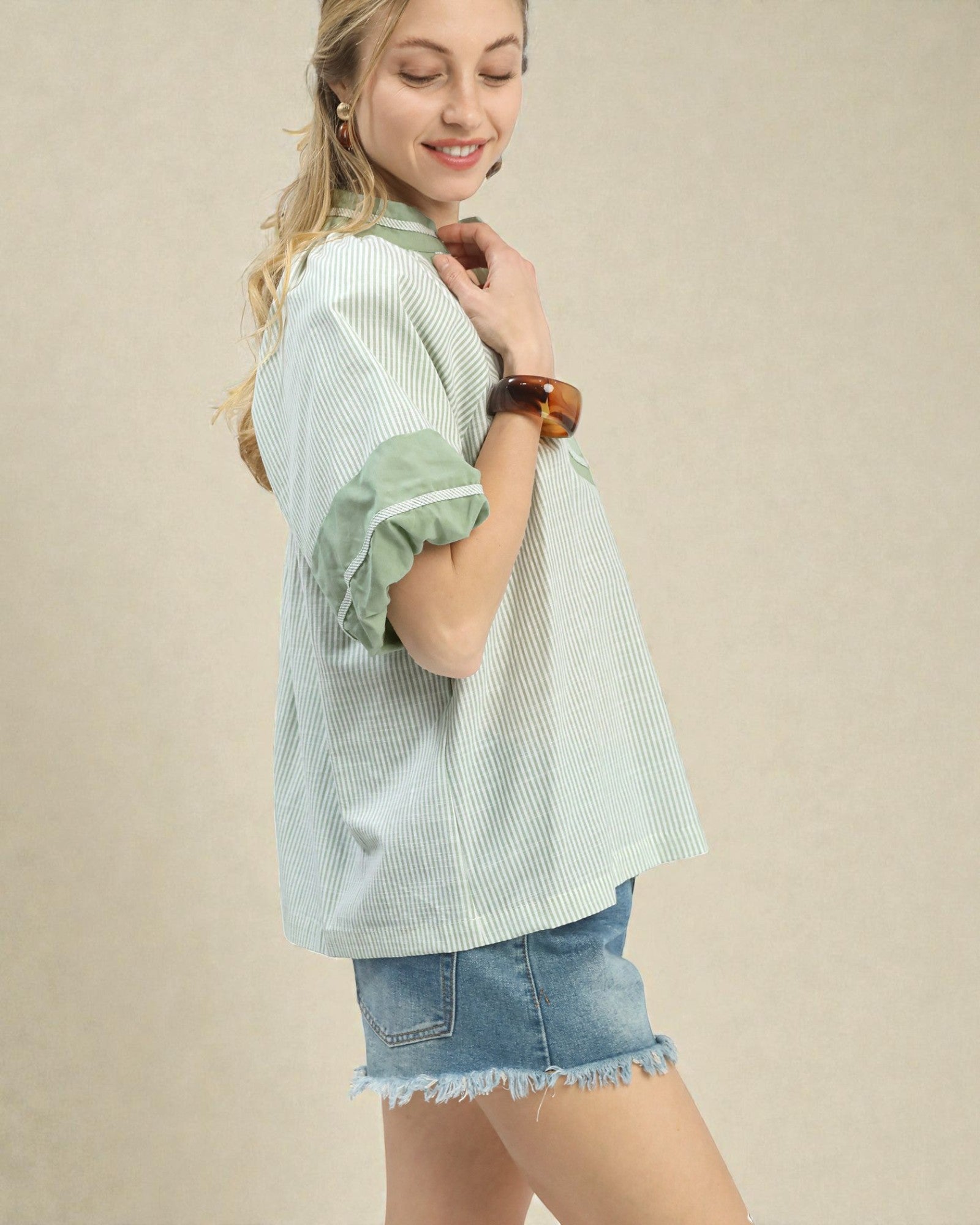 Woman wearing a light green striped shirt and denim shorts on a beige background