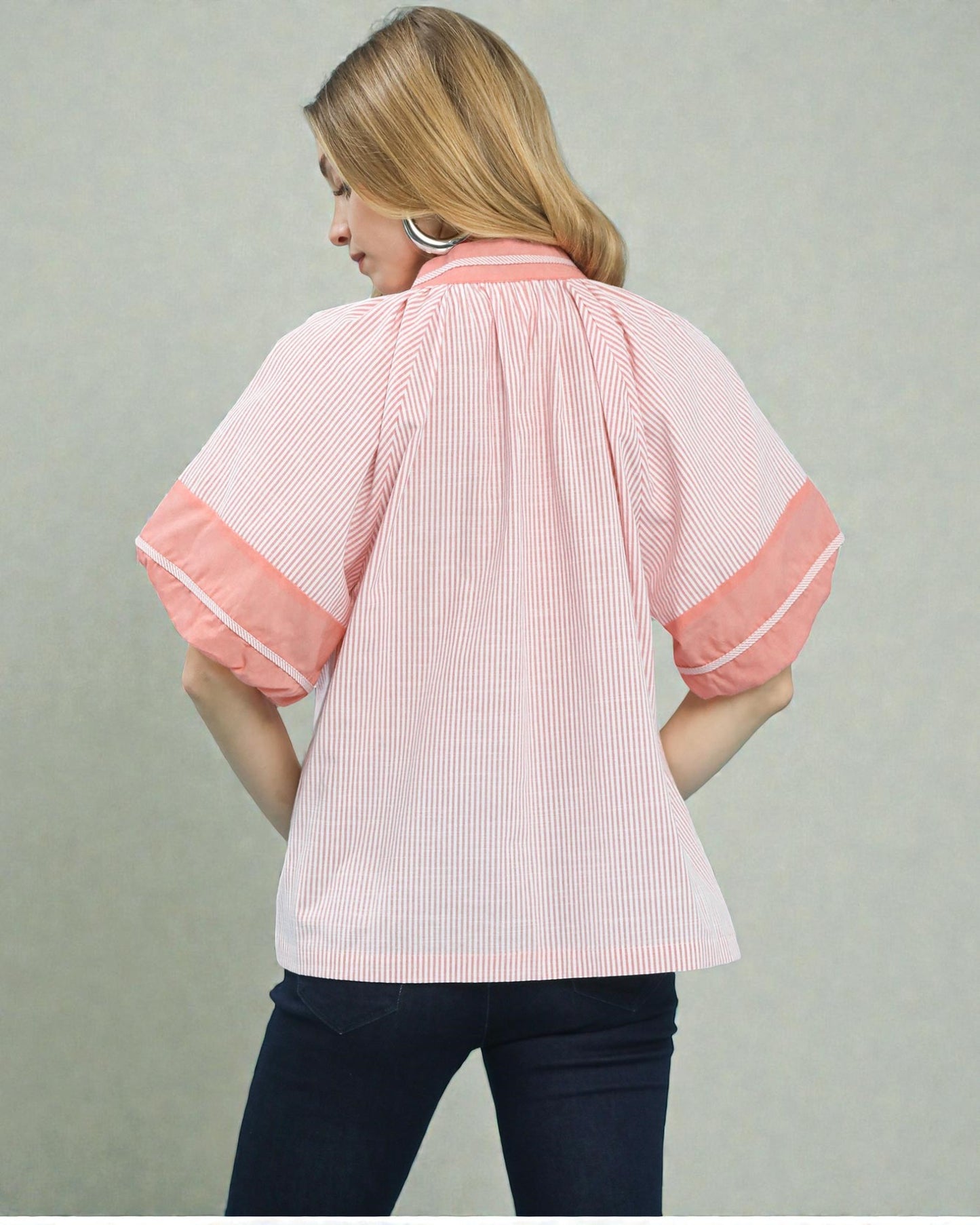 Woman wearing a pink and white striped shirt with rolled-up sleeves on a plain background