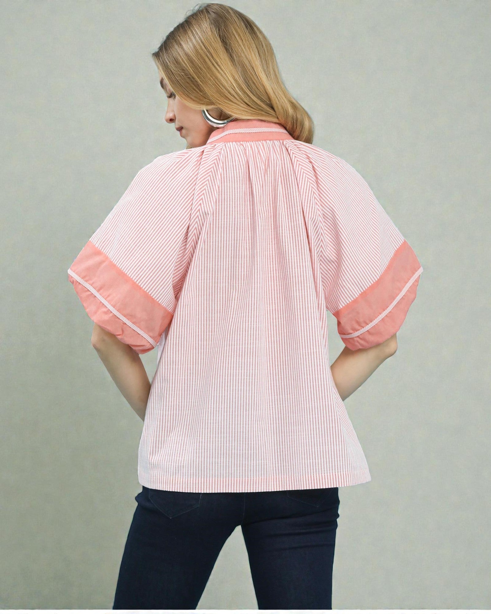 Woman wearing a pink and white striped shirt with rolled-up sleeves on a plain background