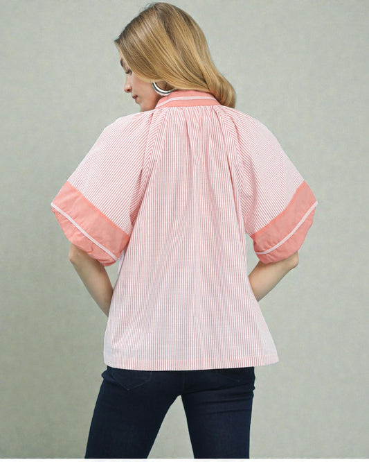 Woman wearing a pink and white striped shirt with rolled-up sleeves on a plain background