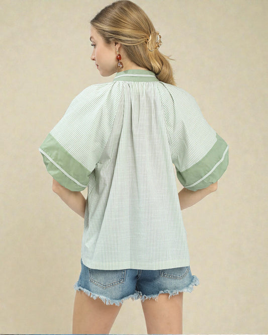 Woman wearing a light green and white striped shirt with denim shorts on a beige background