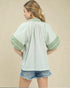 Woman wearing a light green and white striped shirt with denim shorts on a beige background