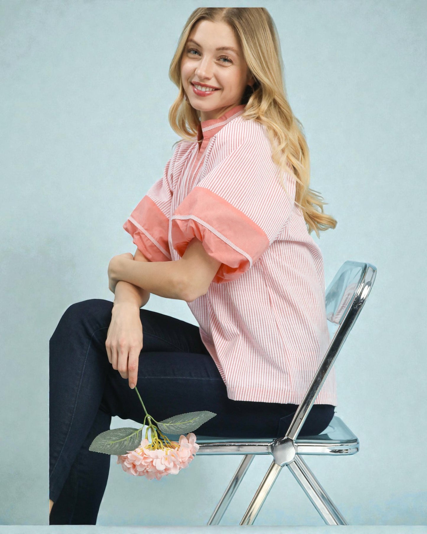 Woman sitting on a chair holding a pink flower against a light blue background