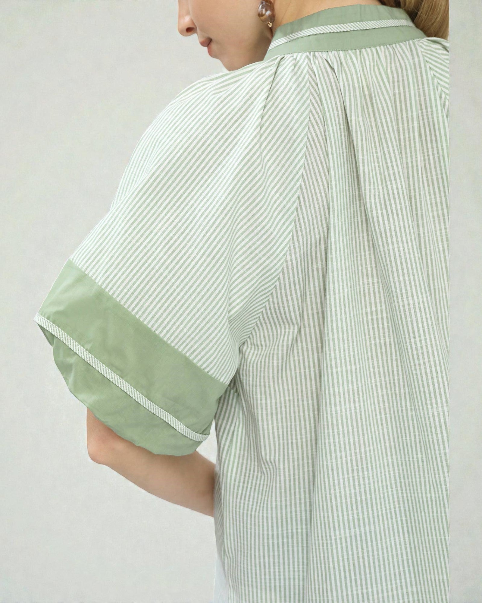 Green and white striped shirt worn by a person on a plain background