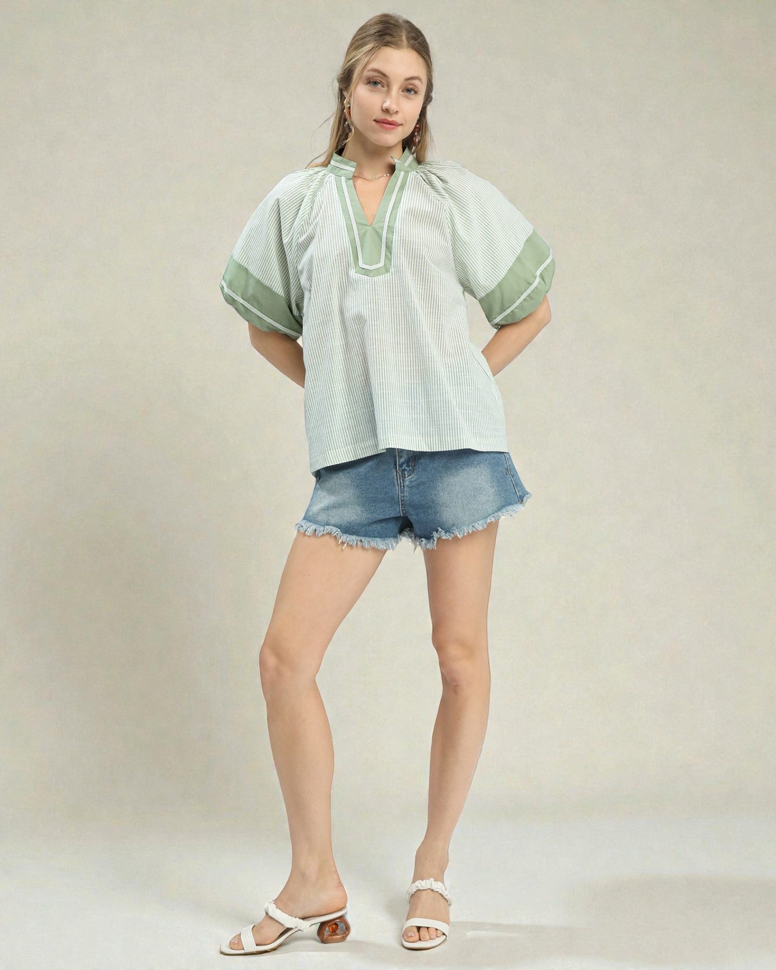 Woman wearing a light green blouse with short sleeves and denim shorts on a plain background