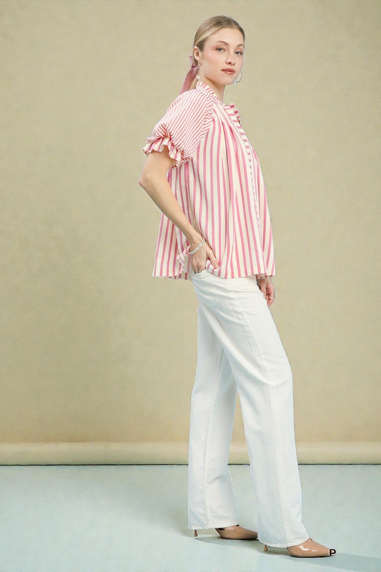 Woman wearing a red and white striped shirt with ruffled sleeves and white pants against a beige background