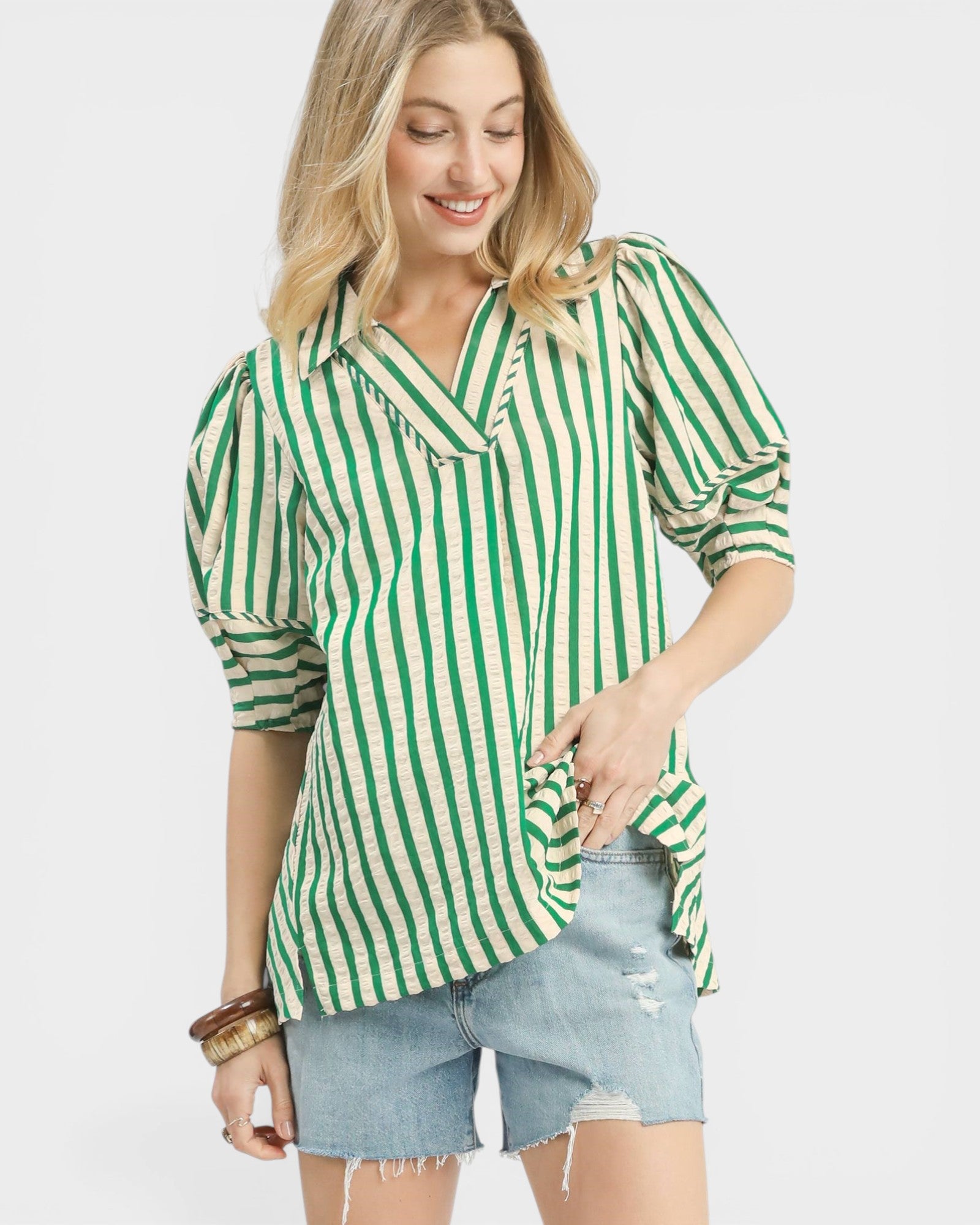 Woman wearing a green and white striped shirt with denim shorts on a light gray background