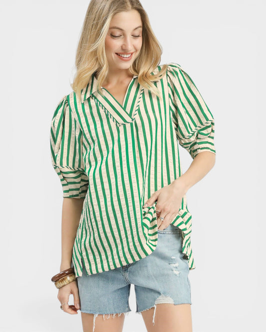 Woman wearing a green and white striped shirt with denim shorts on a light gray background