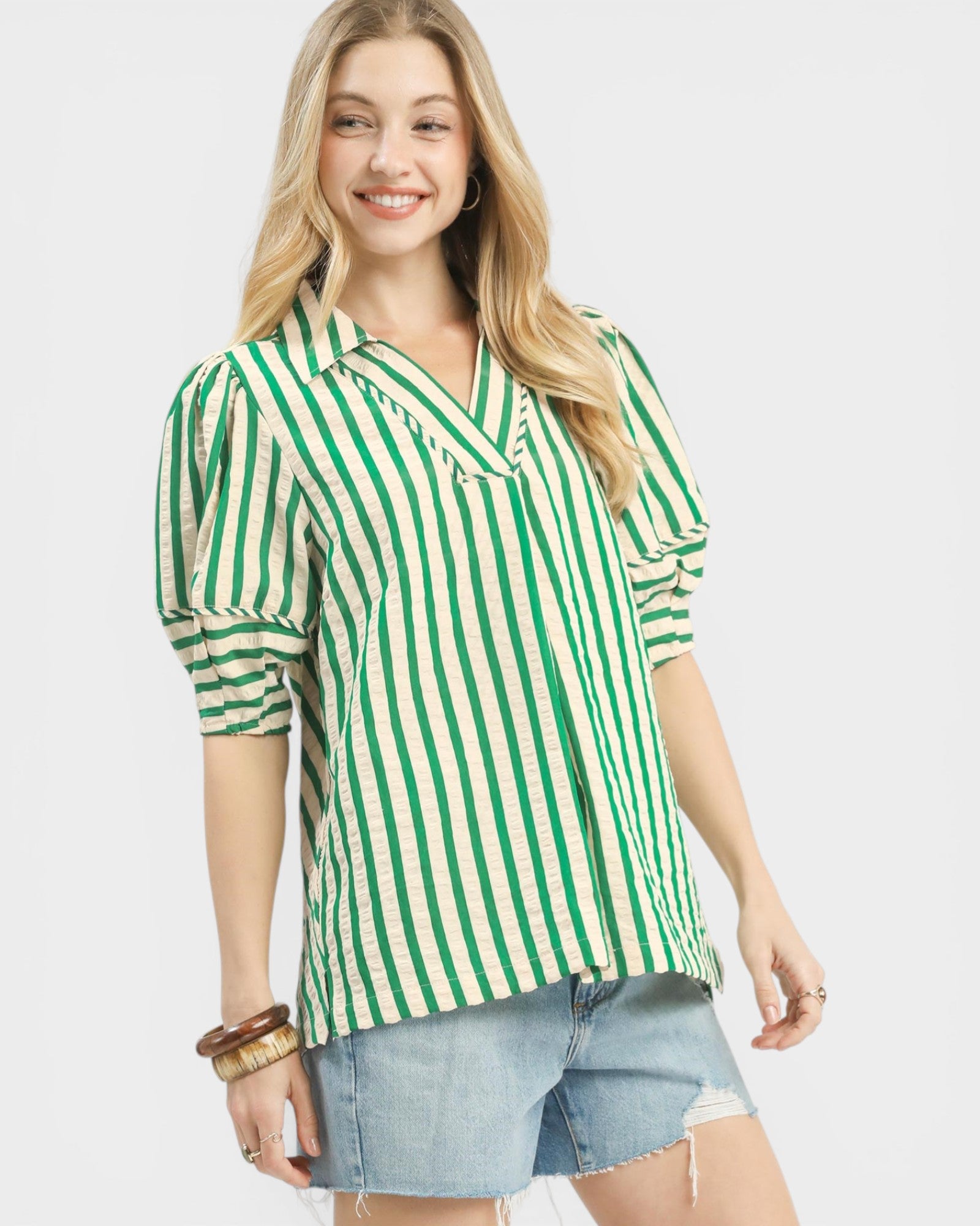 Woman wearing a green and white striped shirt with denim shorts on a plain background