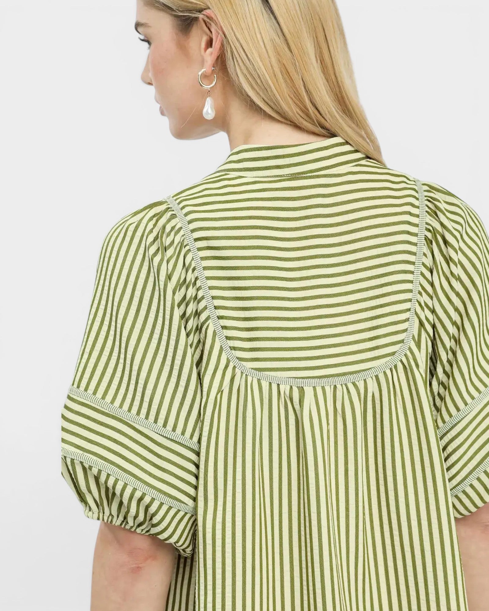 Green and white striped shirt worn by a person on a plain background