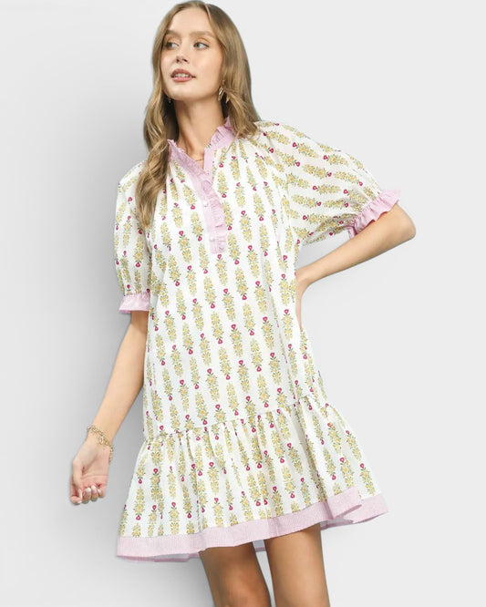 Woman wearing a patterned dress with pink trim on a plain background