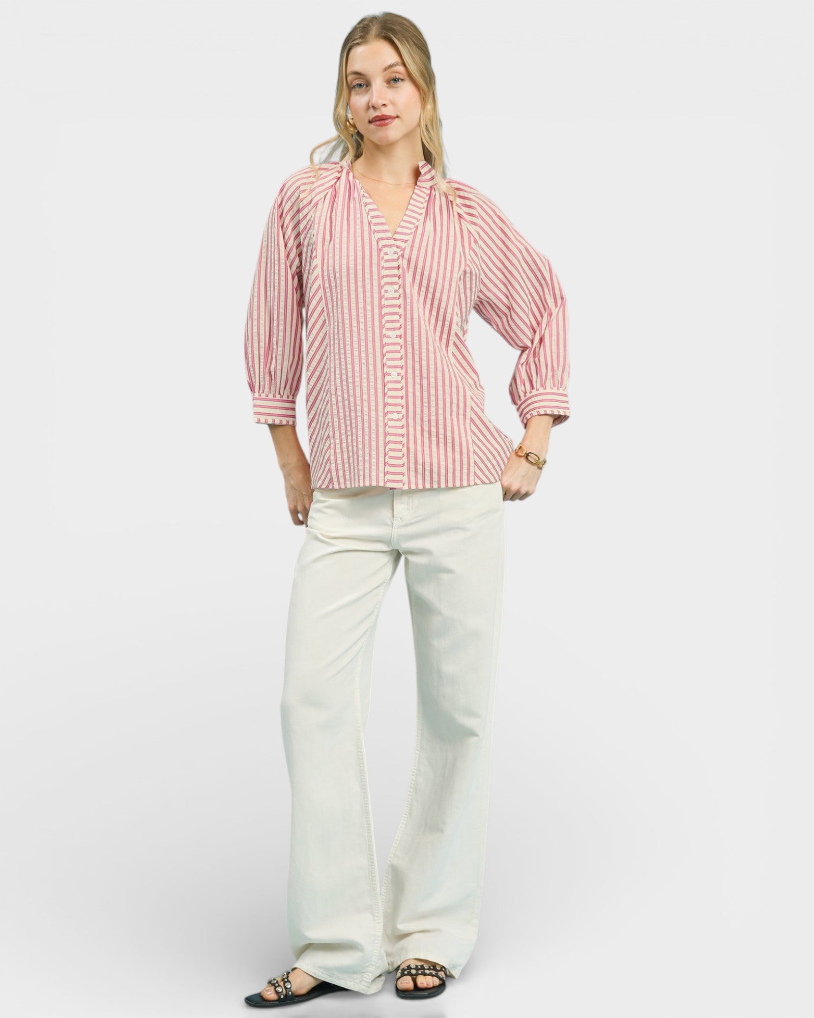 Woman wearing a pink and white striped shirt and white pants on a plain background