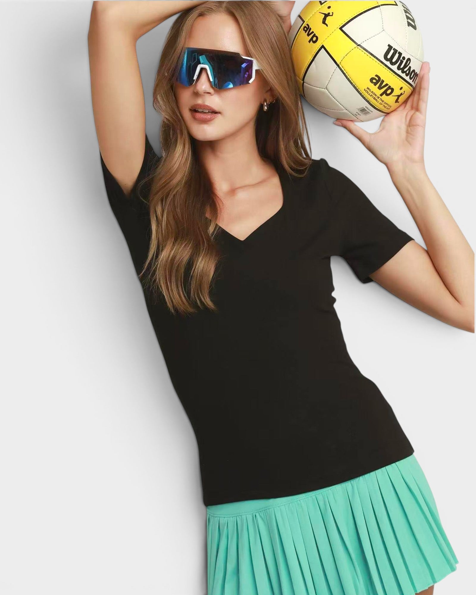 Woman wearing a black top and green skirt holding a volleyball against a light gray background