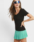 Woman wearing a black top and teal pleated skirt with reflective sunglasses on a white background