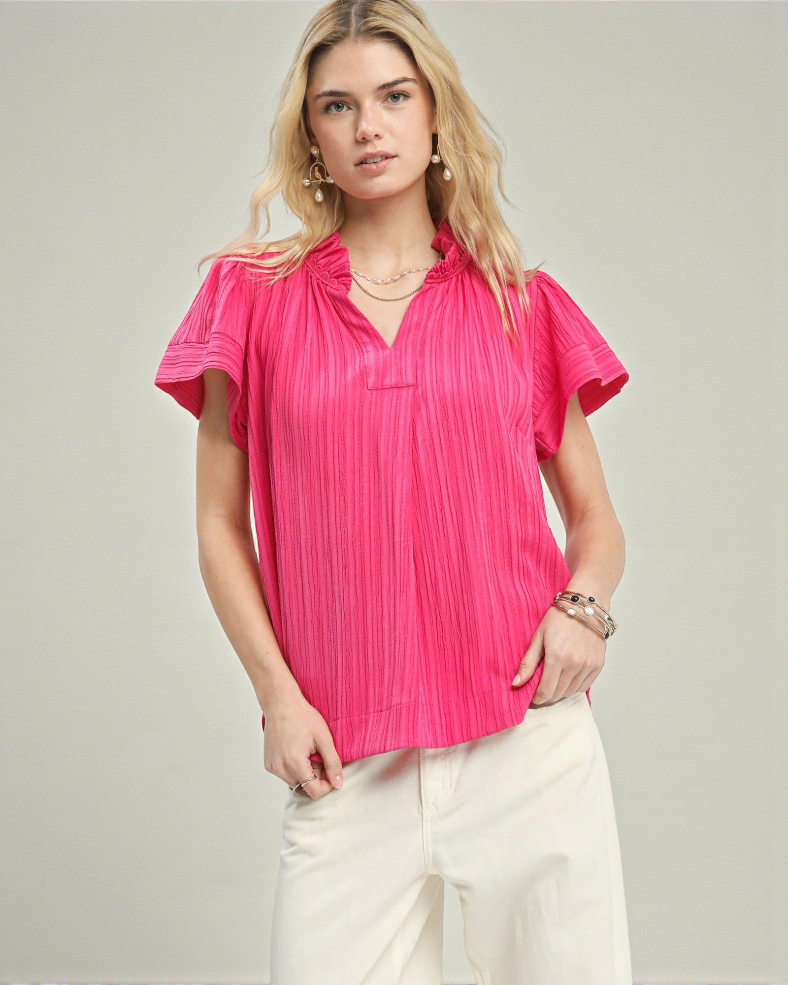 Woman wearing a bright pink blouse with short sleeves on a plain background