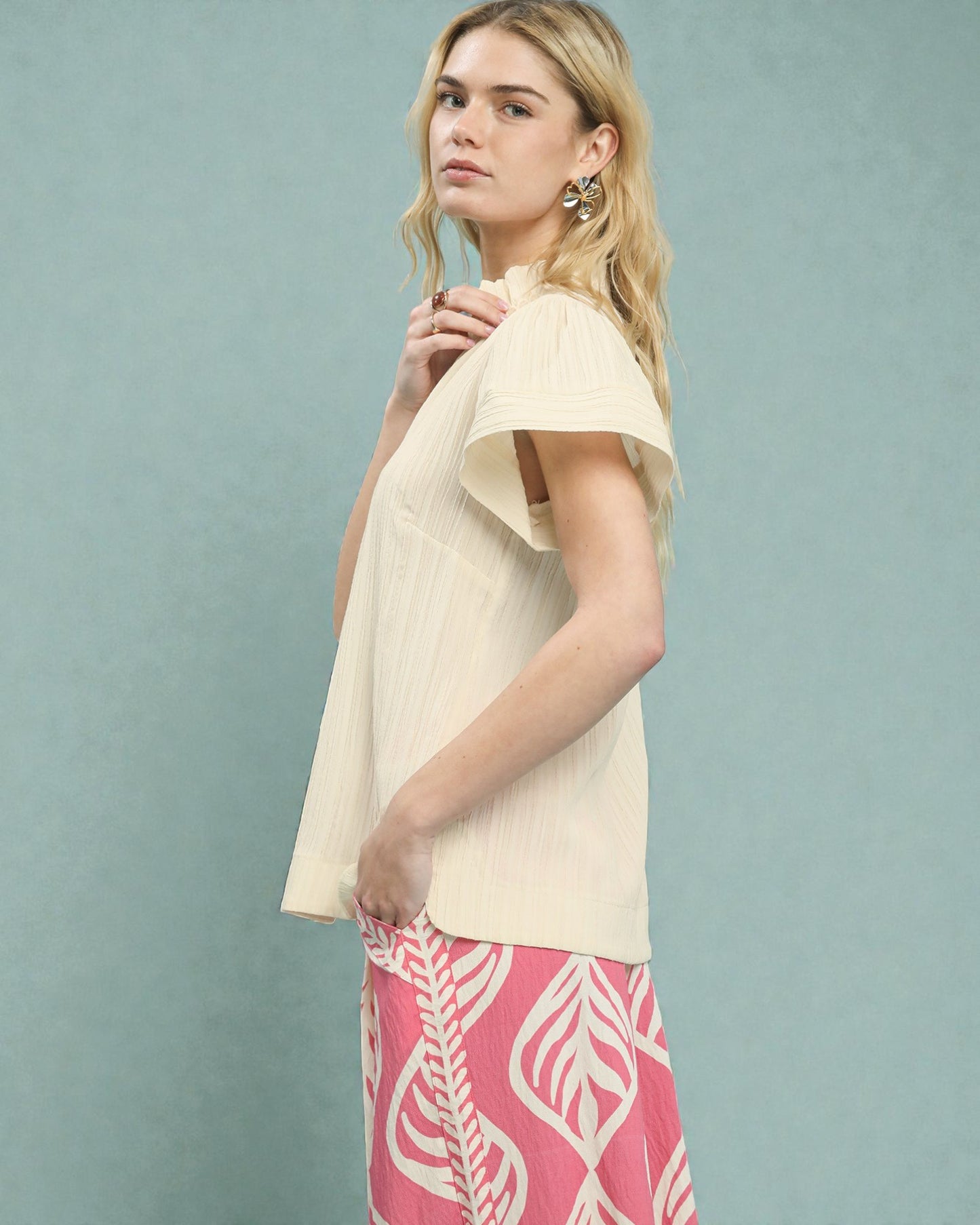 Woman wearing a beige top and pink patterned pants against a light blue background