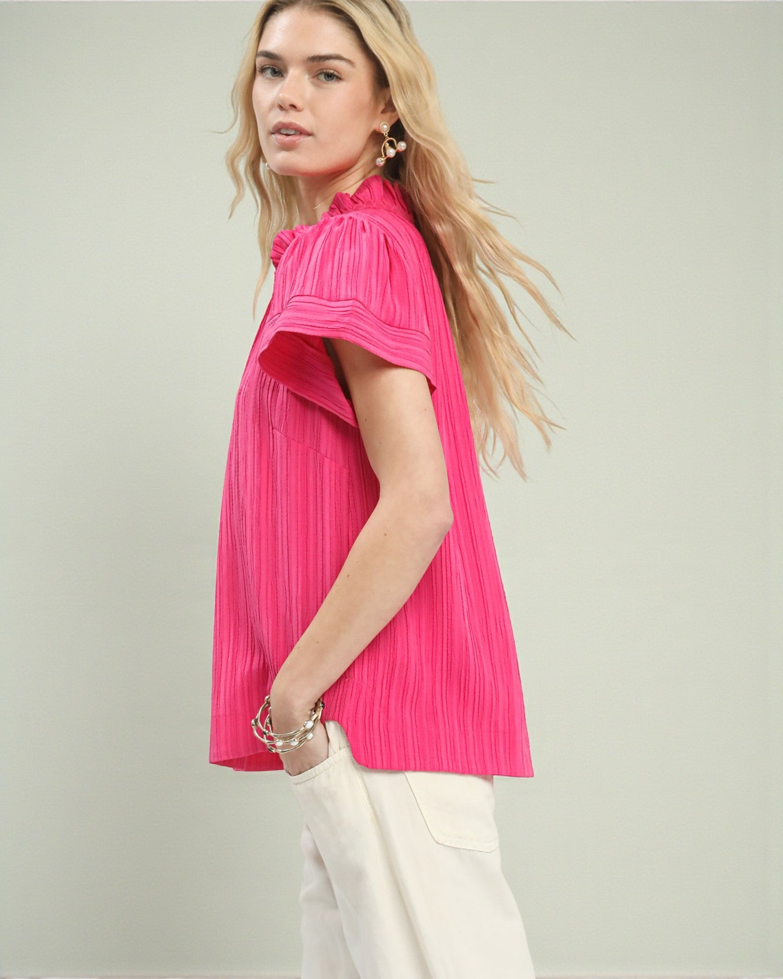 Woman wearing a bright pink pleated top against a light background