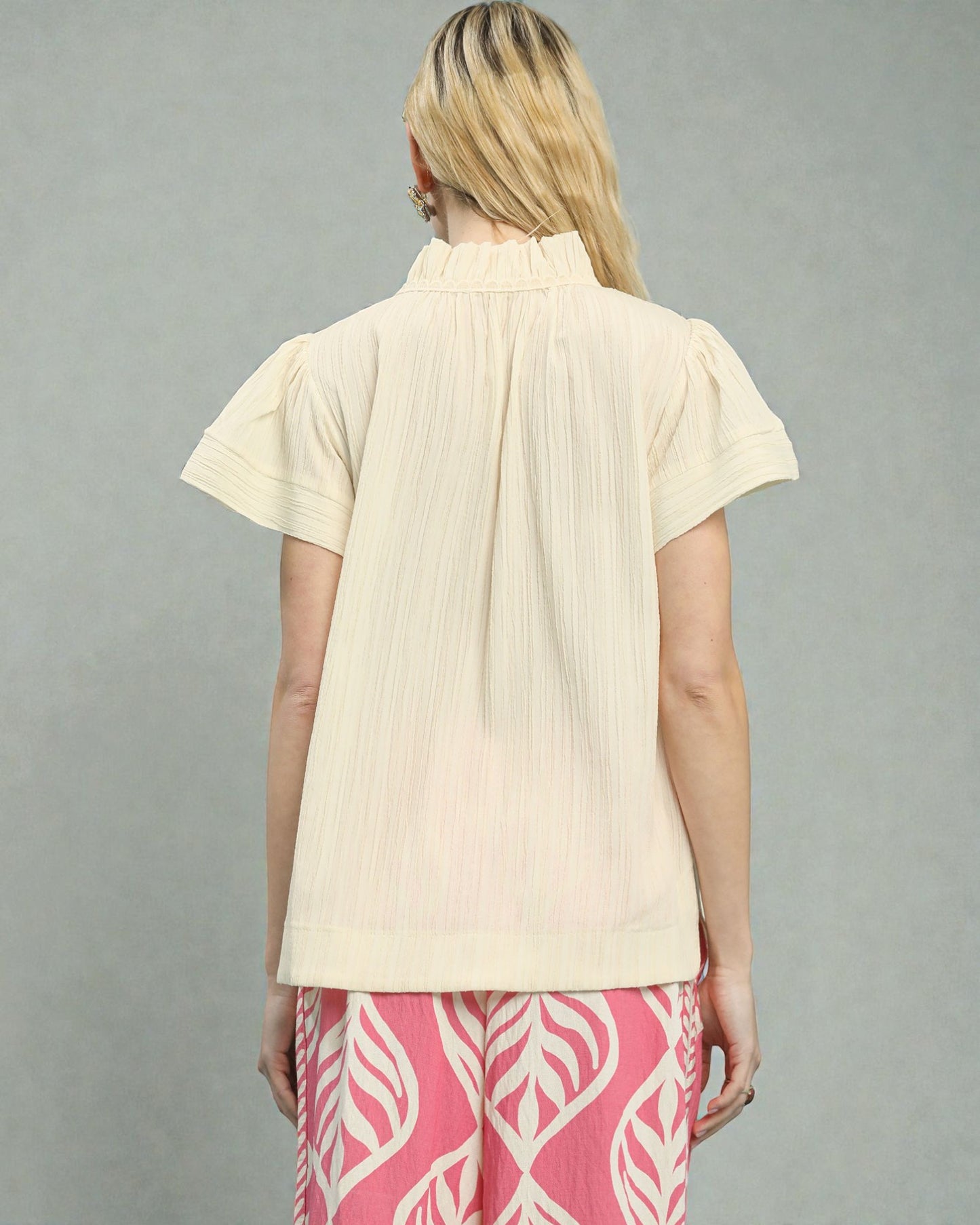 Woman wearing a beige short-sleeve blouse and pink pants with white patterns on a gray background