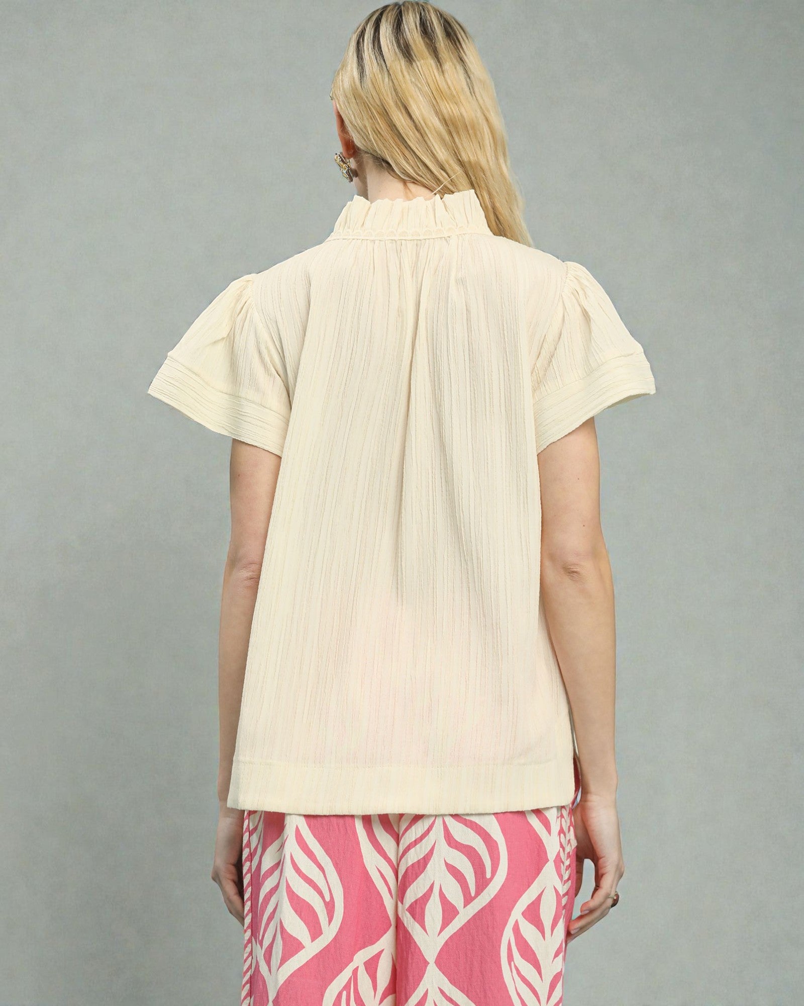 Woman wearing a beige short-sleeve blouse and pink pants with white patterns on a gray background