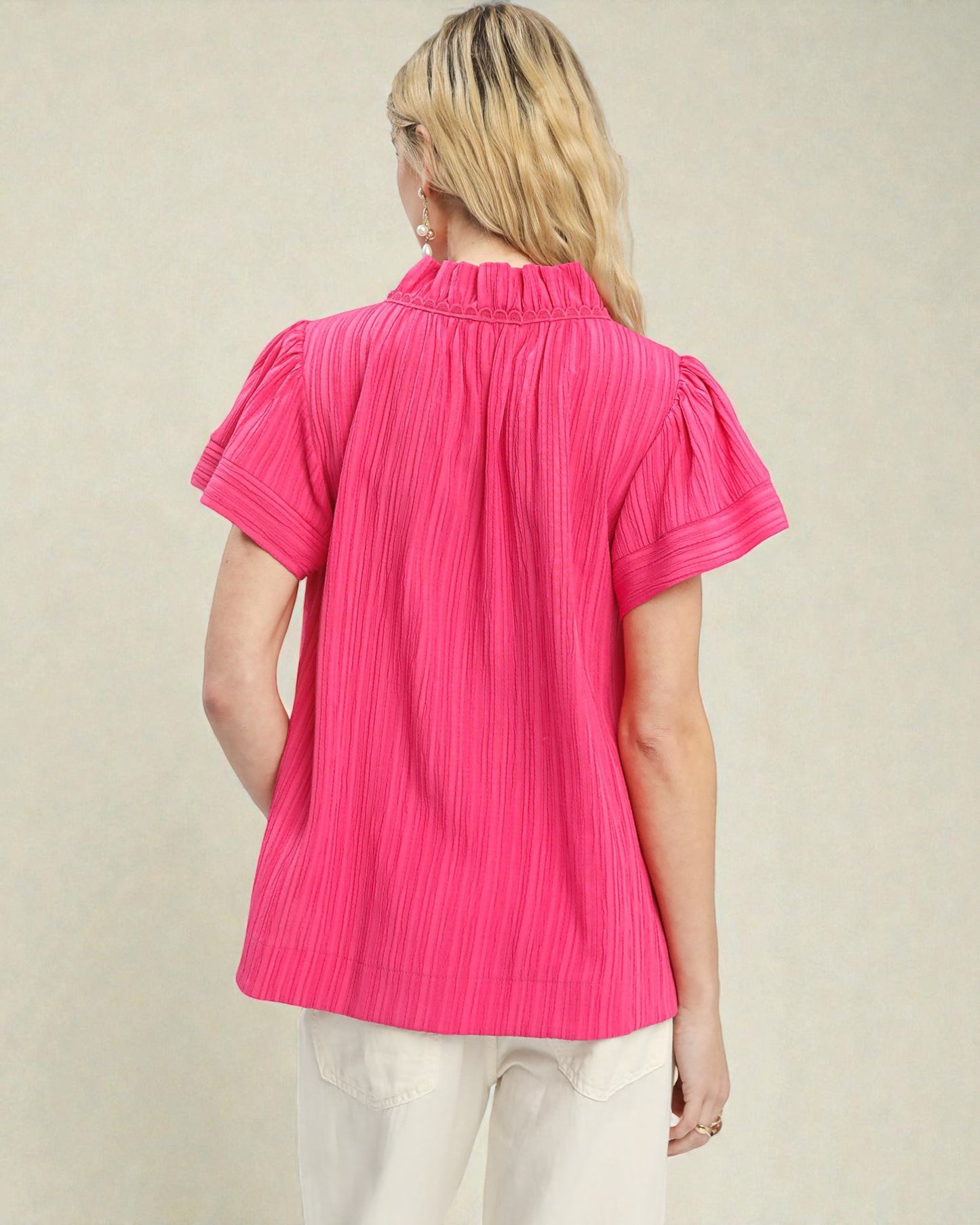 Woman wearing a bright pink pleated blouse against a beige background