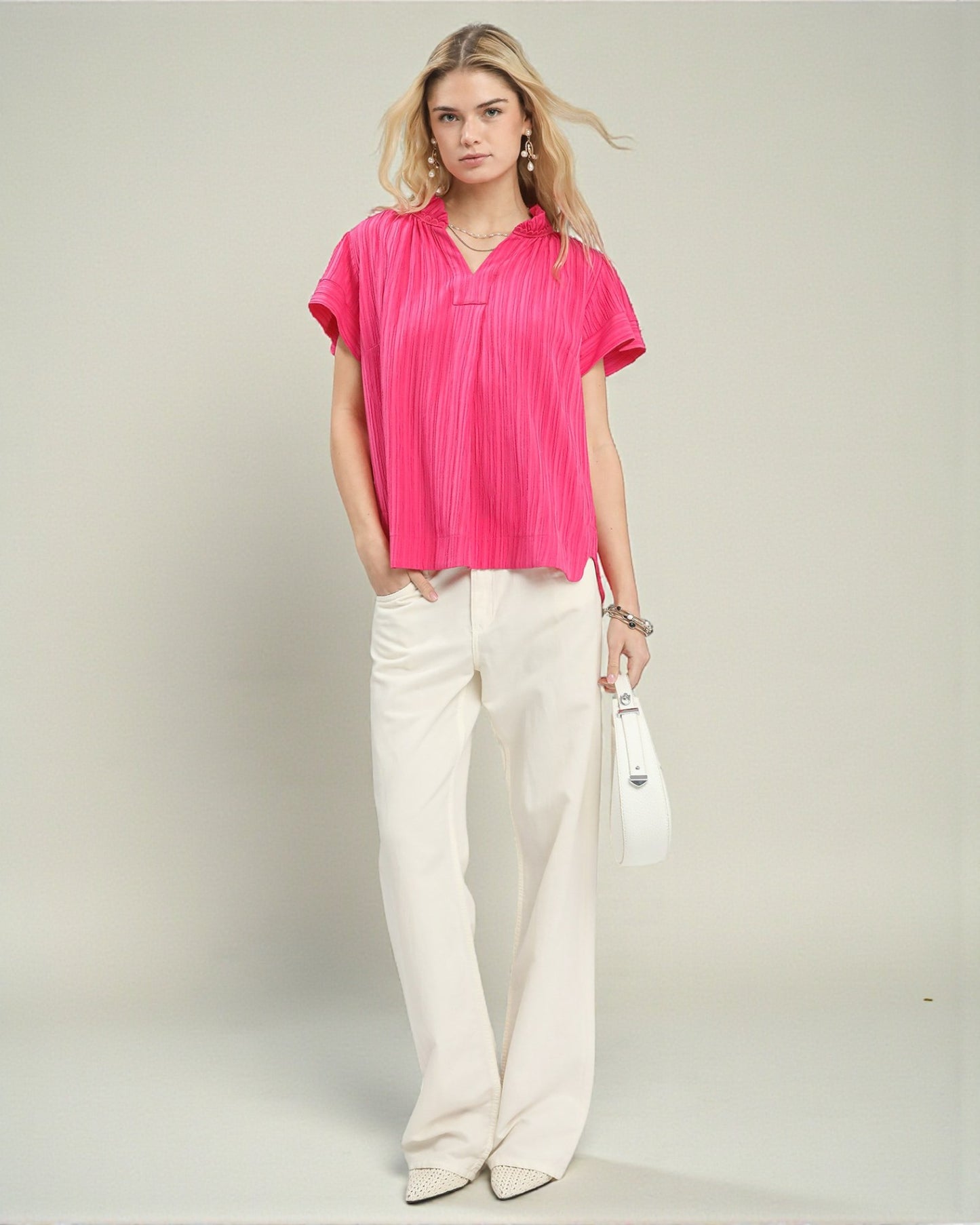 Woman wearing a bright pink blouse and white pants on a plain background