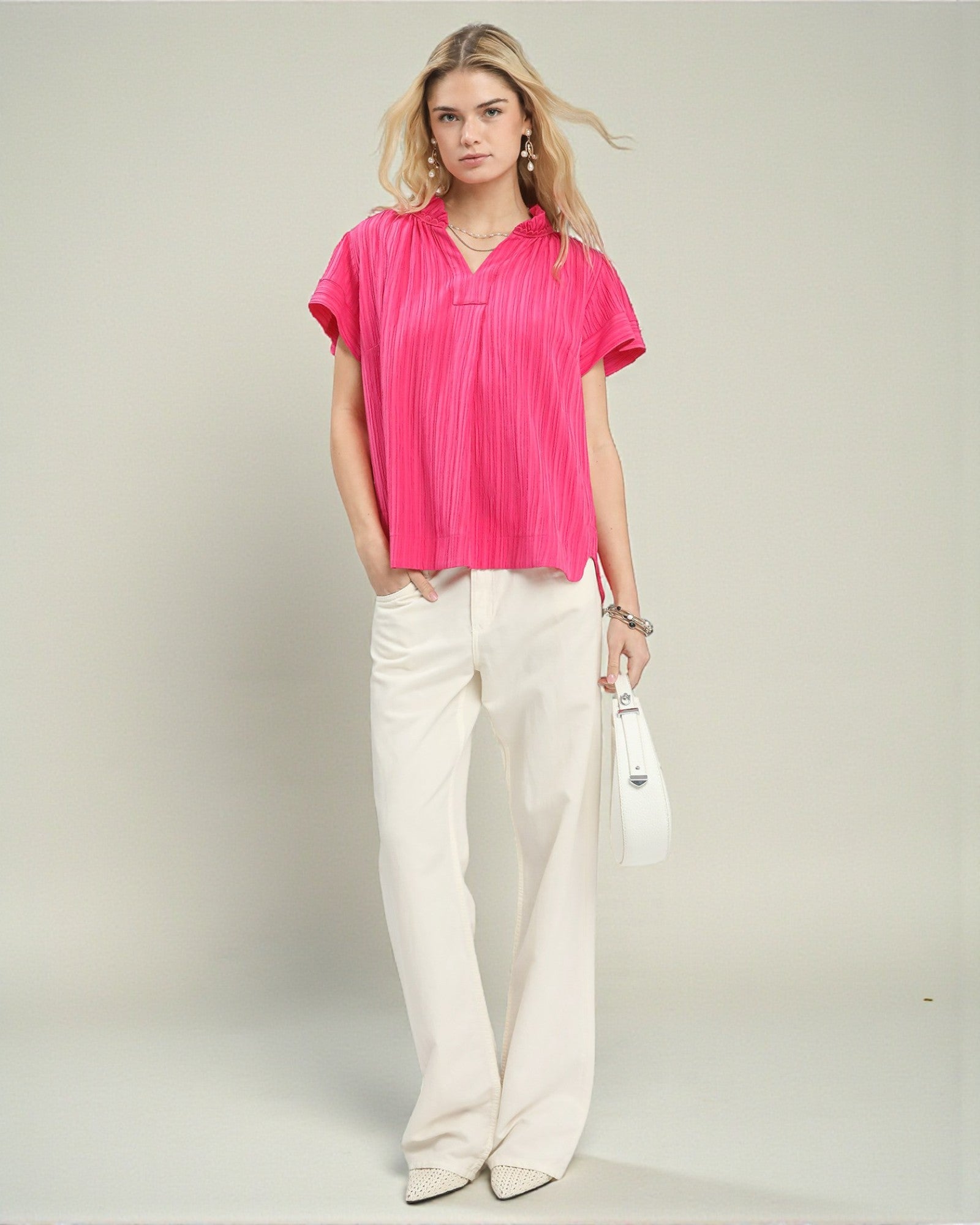 Woman wearing a bright pink blouse and white pants on a plain background
