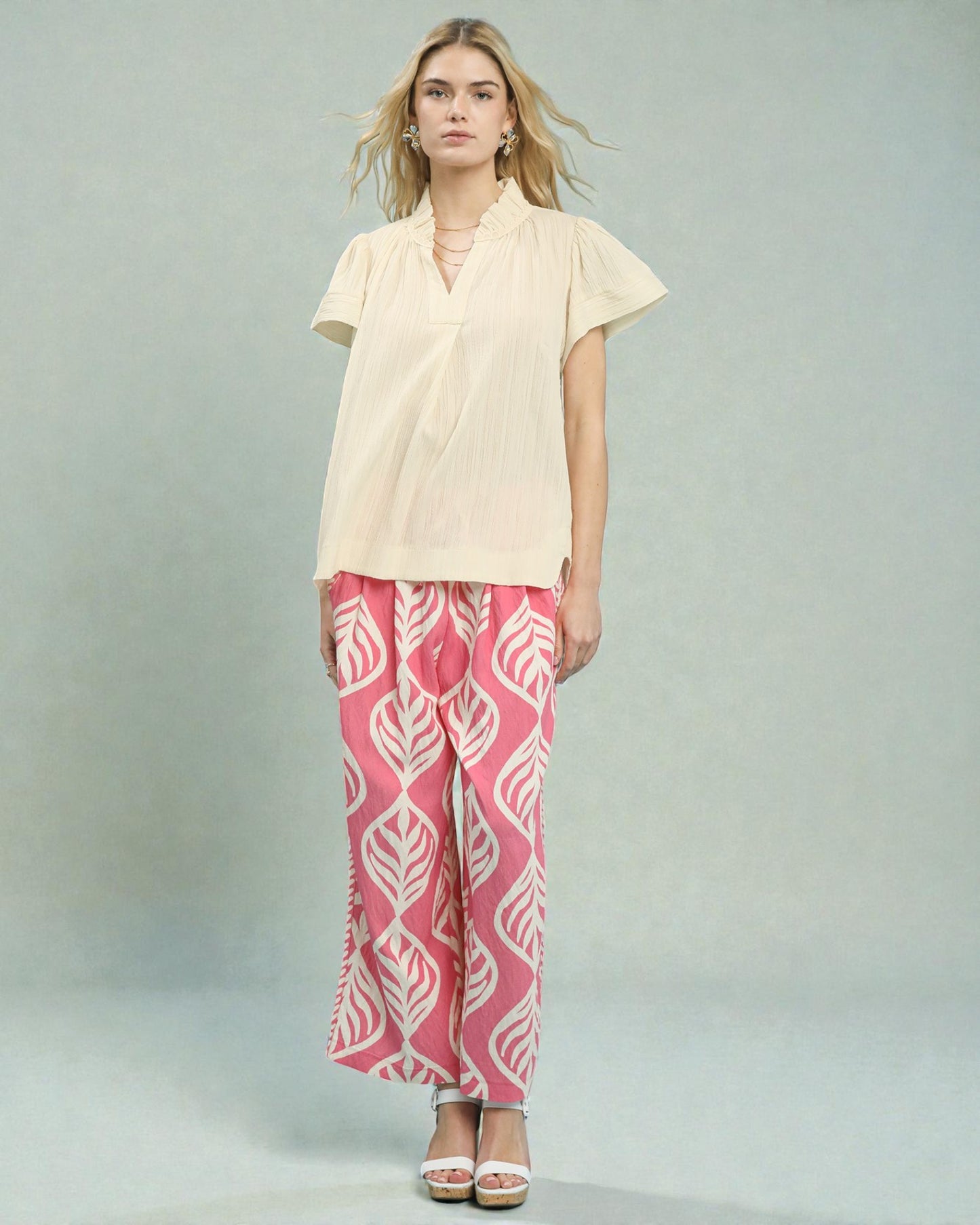 Woman wearing a beige top and pink patterned pants on a gray background