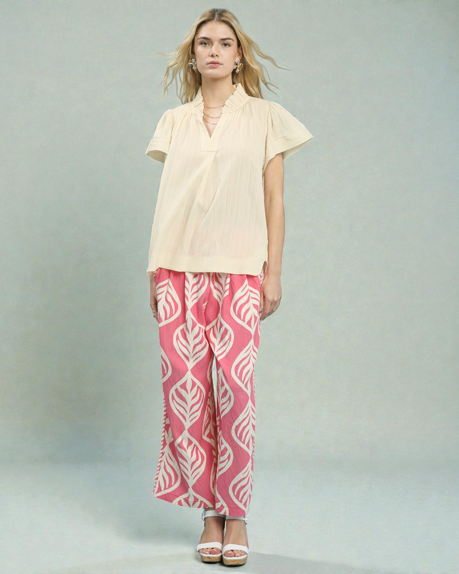 Woman wearing a beige top and pink patterned pants on a gray background