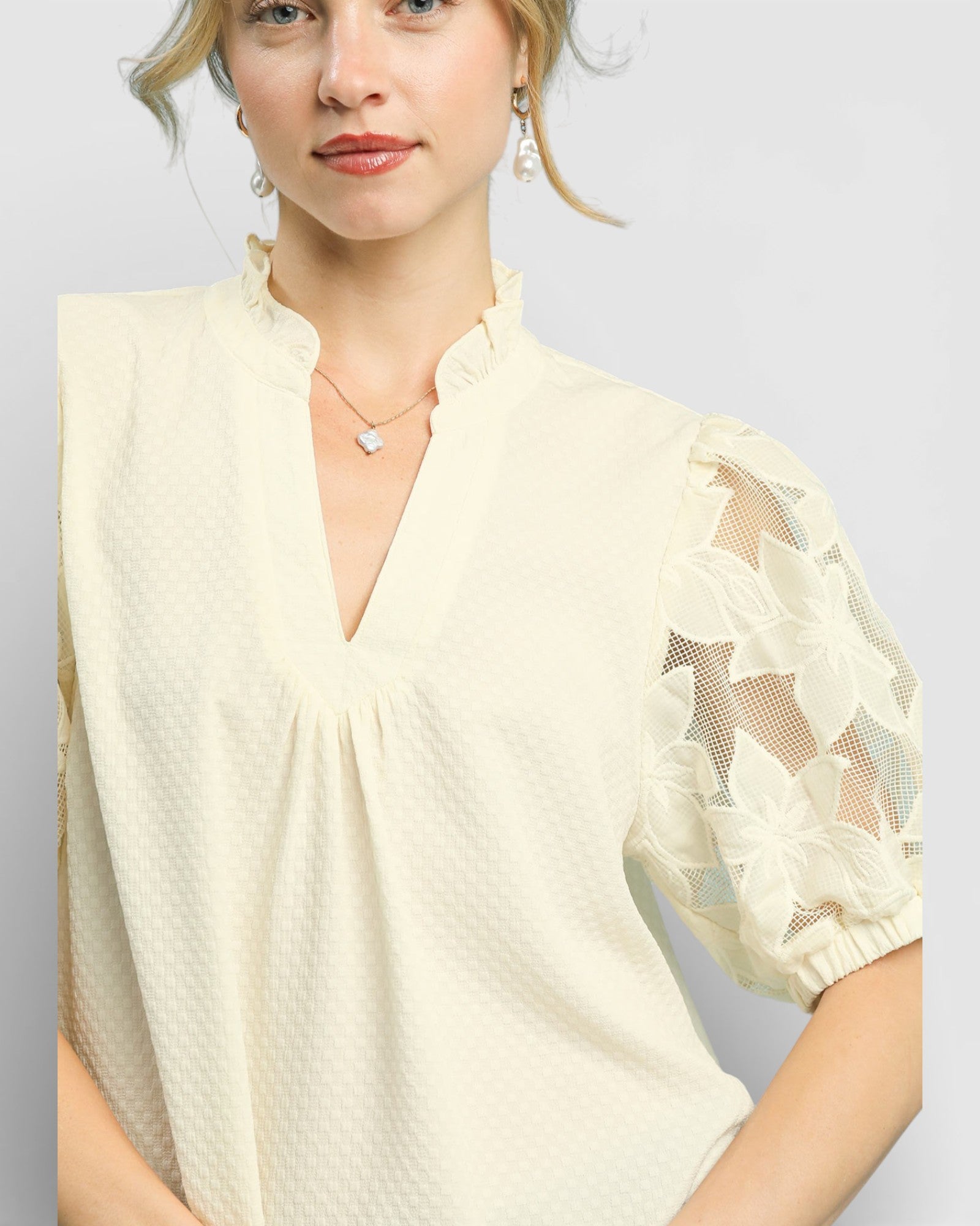 Woman wearing a light-colored blouse with lace sleeves on a plain background