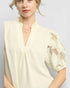 Woman wearing a light-colored blouse with lace sleeves on a plain background