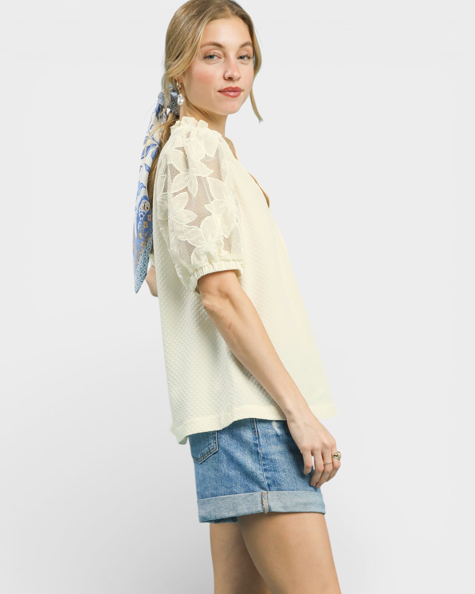Woman wearing a light-colored blouse and denim shorts with a scarf on a white background