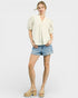 Woman wearing a light-colored blouse with lace sleeves and denim shorts on a white background