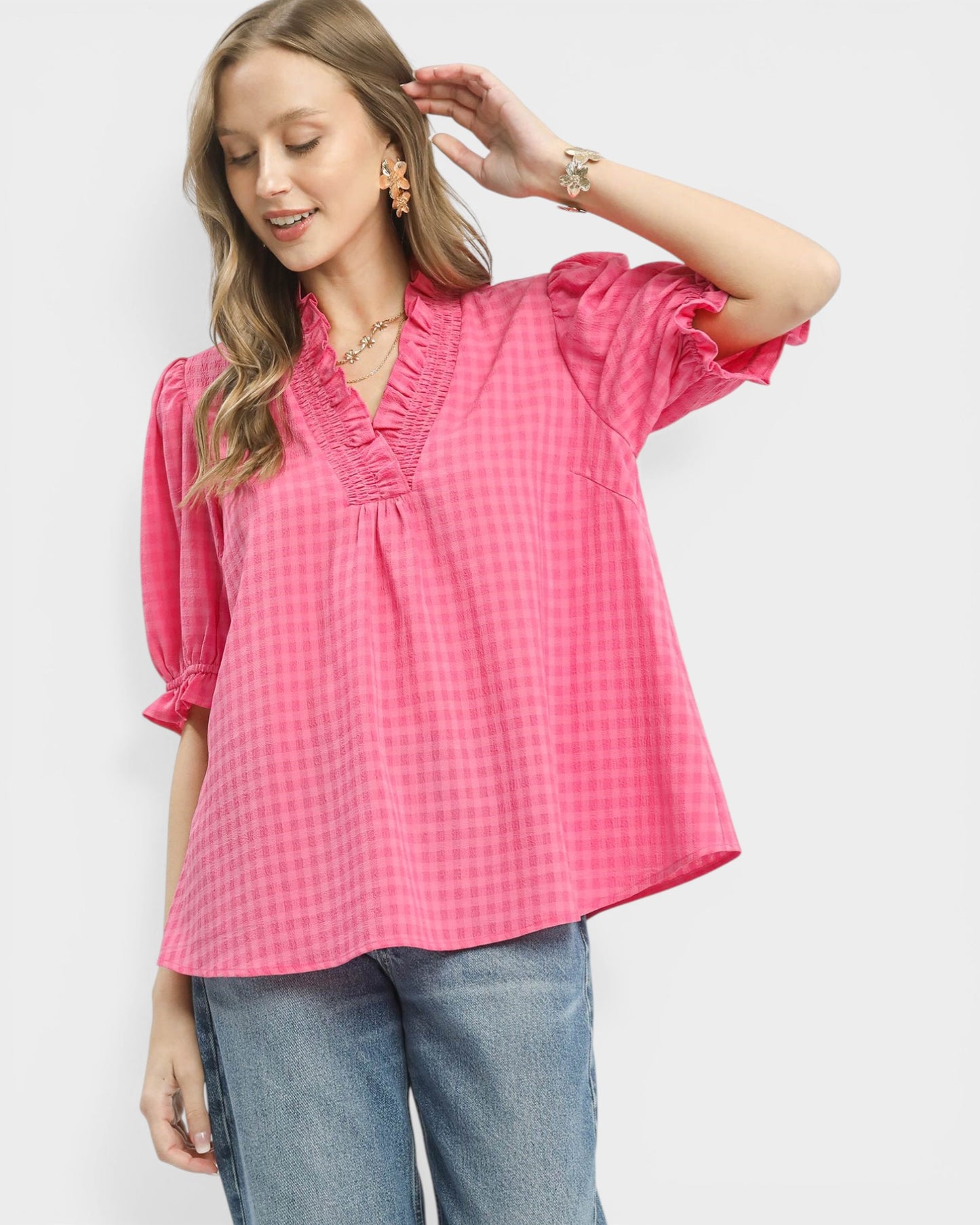 Woman wearing a pink checkered blouse with ruffled sleeves against a white background