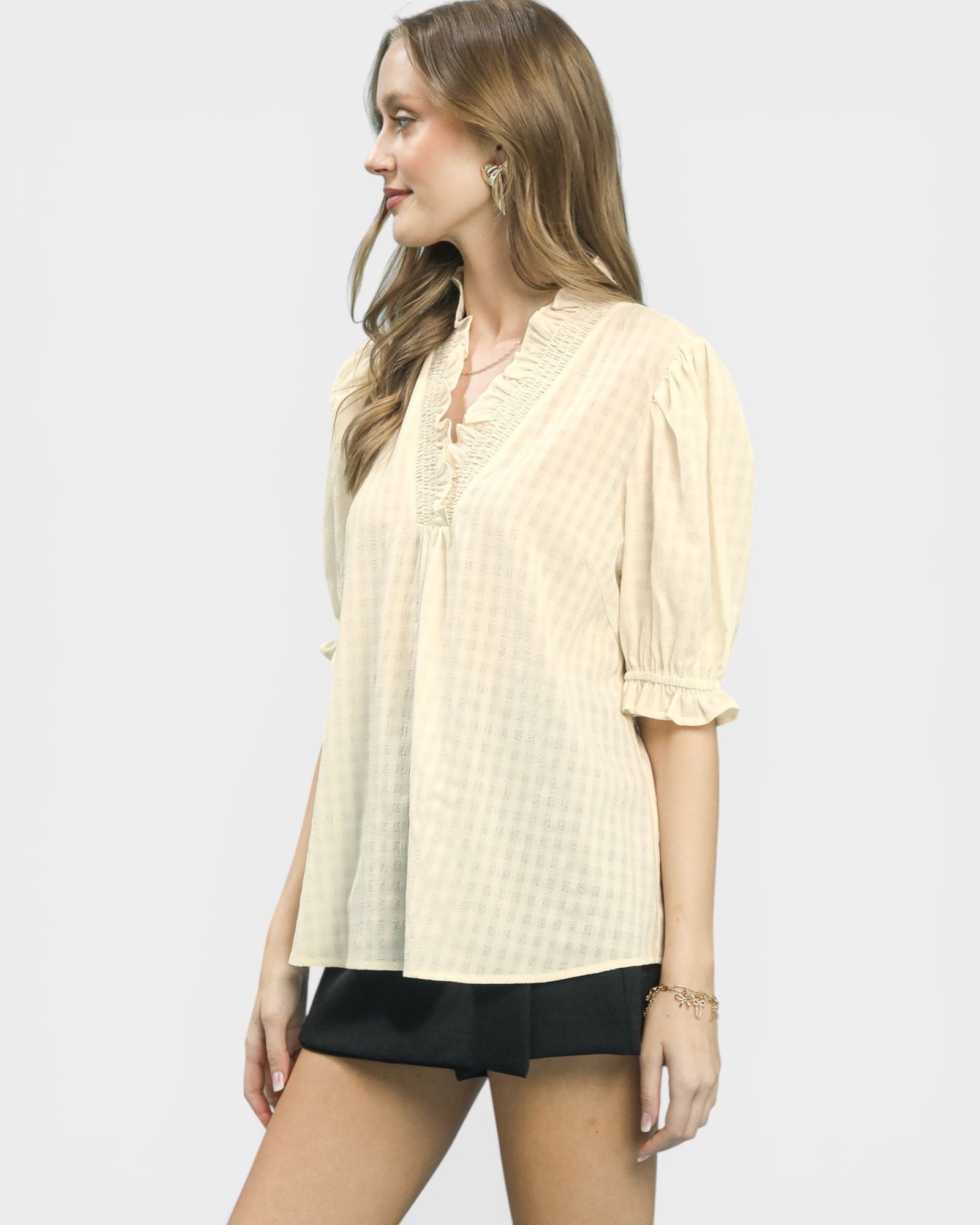 Woman wearing a light yellow blouse and black shorts on a white background