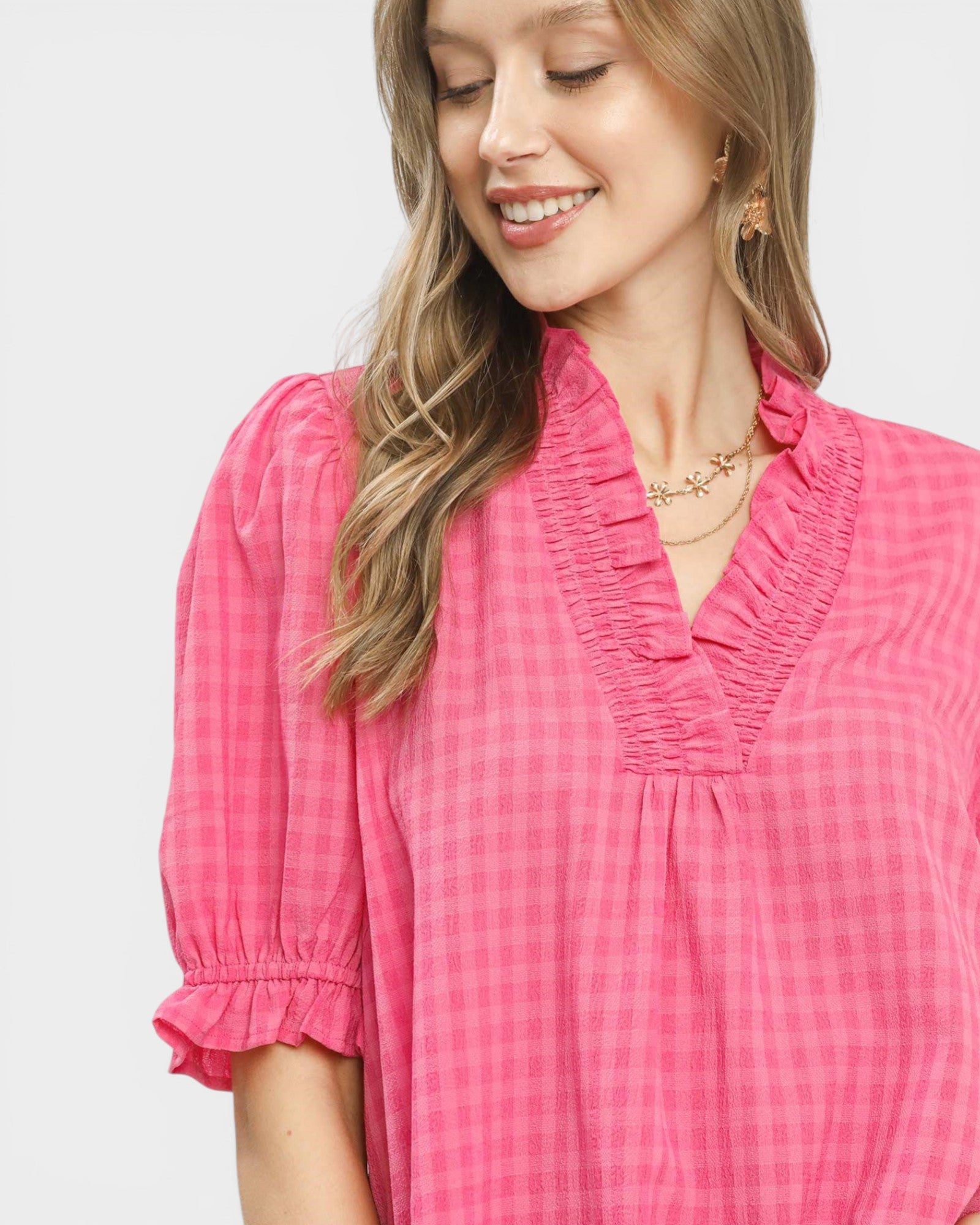 Woman wearing a pink checkered blouse against a light gray background