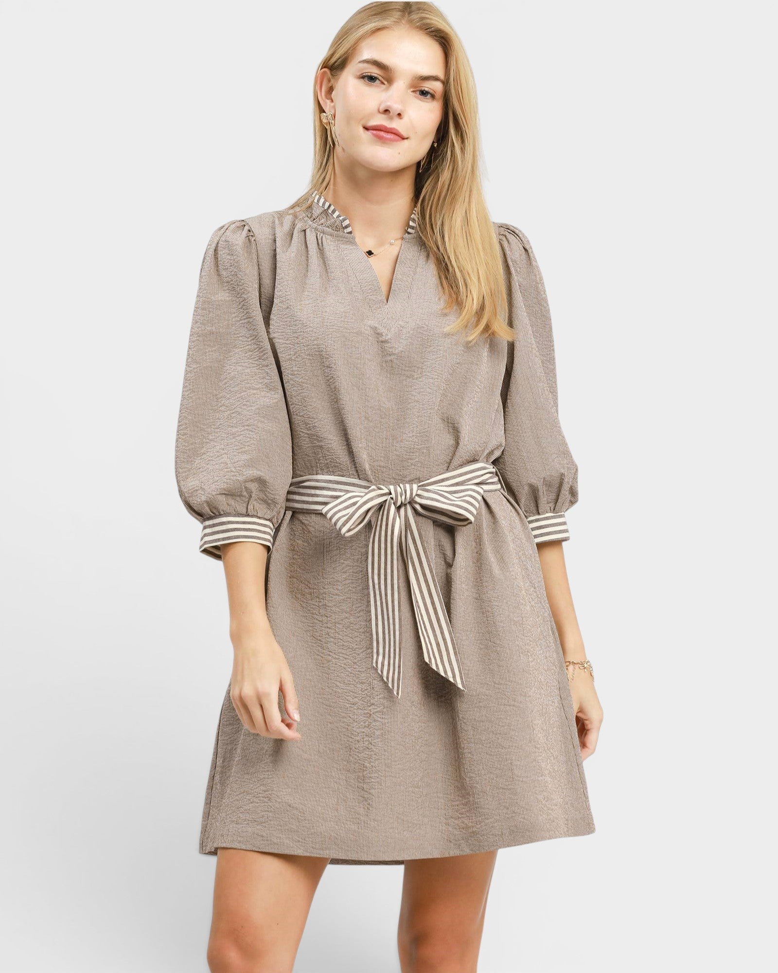 Woman wearing a beige dress with a striped belt on a white background