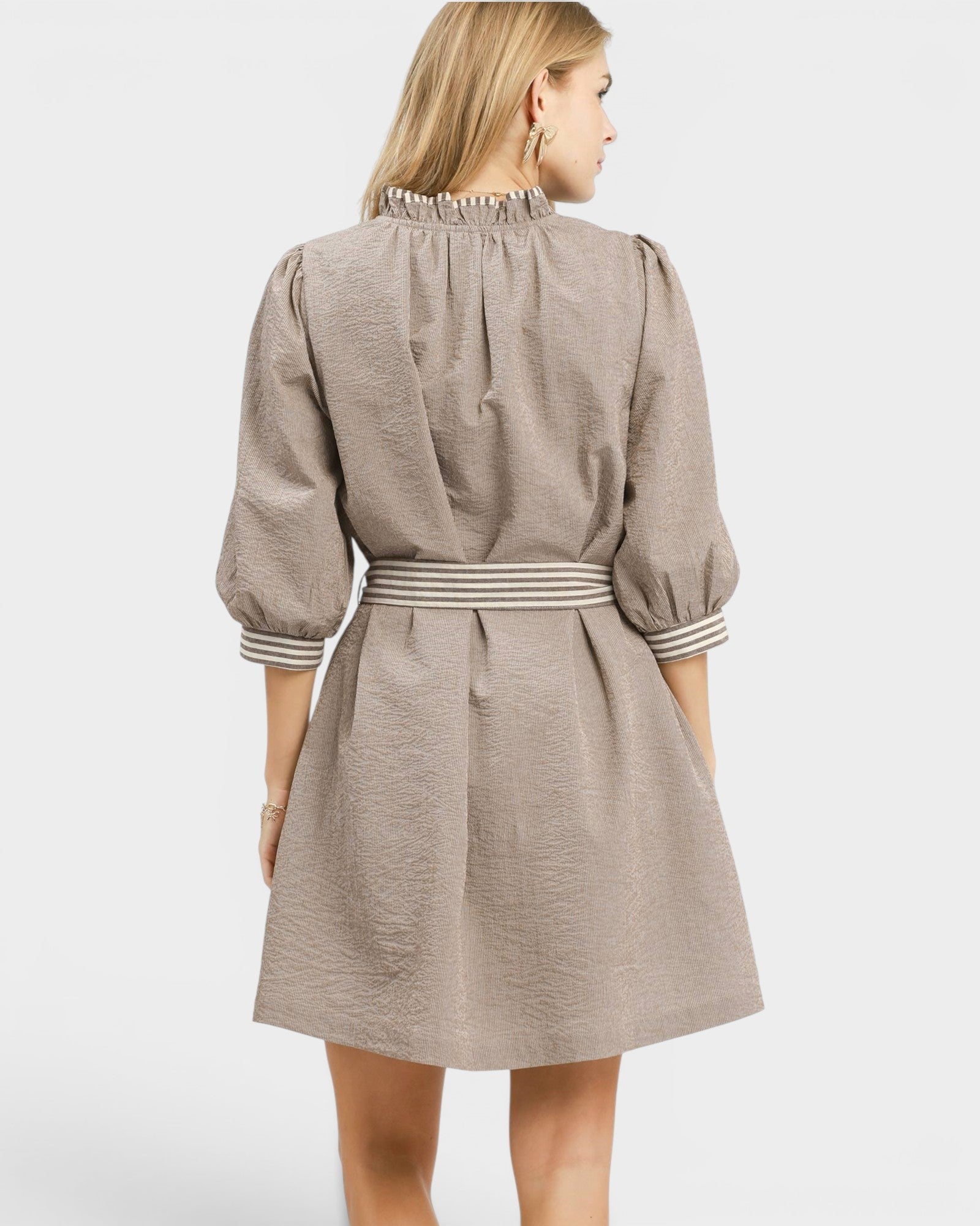 Woman wearing a beige dress with striped trim on a white background