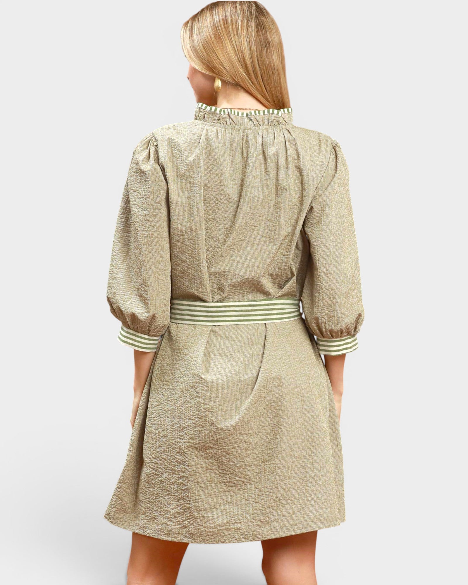 Woman wearing a beige dress with striped trim on a white background