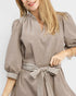 Woman wearing a brown dress with striped belt against a white background