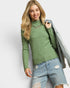 Woman wearing a green textured sweater and denim shorts against a light gray background