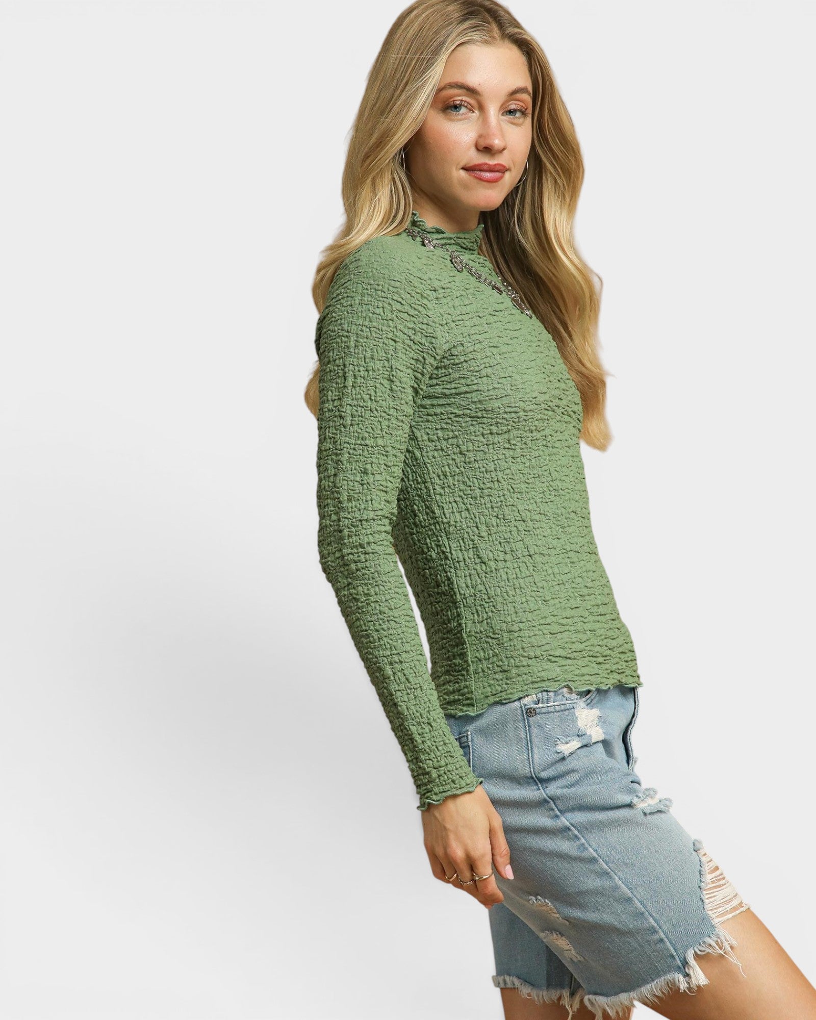 Woman wearing a green textured sweater and denim shorts on a white background