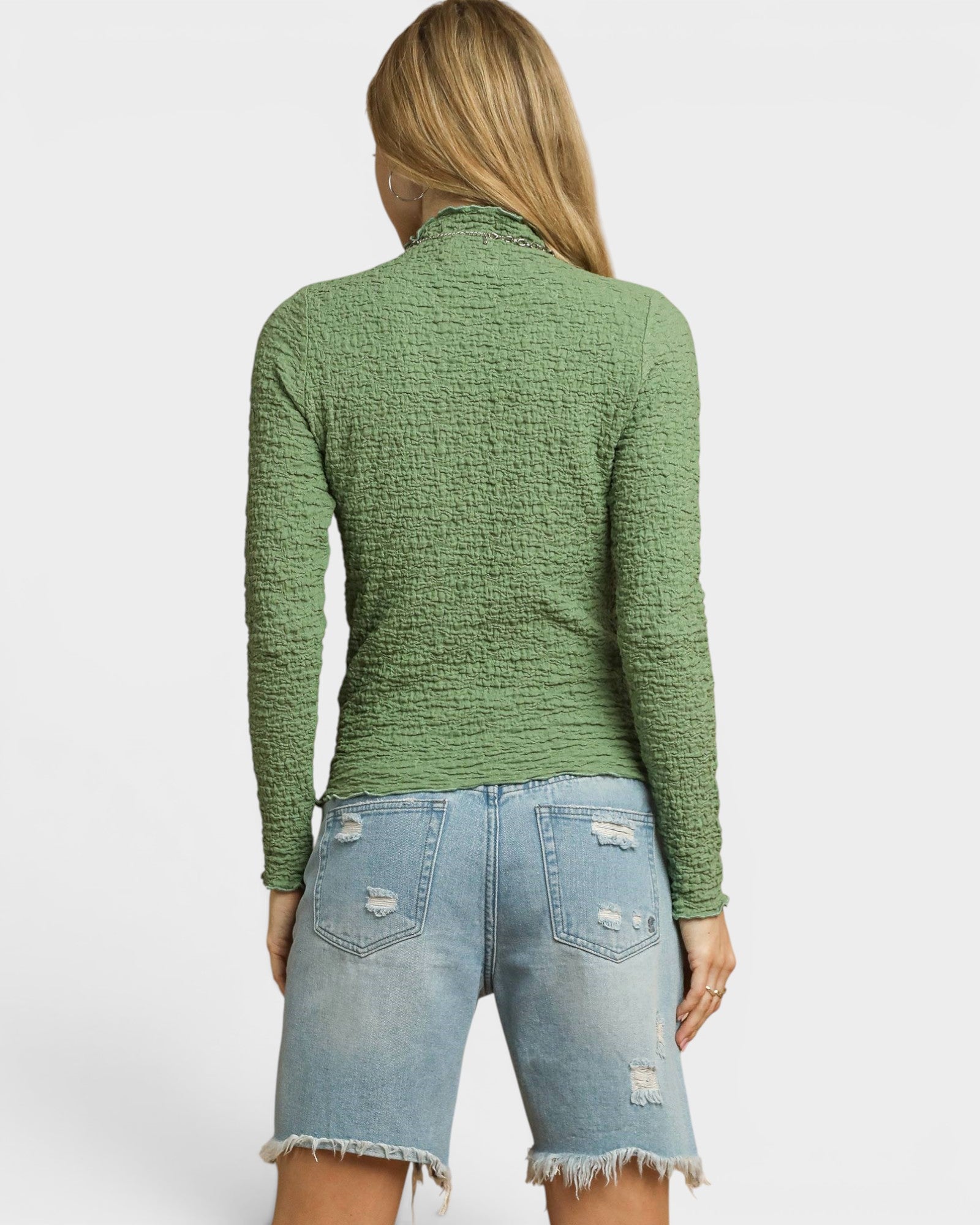 Person wearing a green textured sweater and denim shorts on a white background