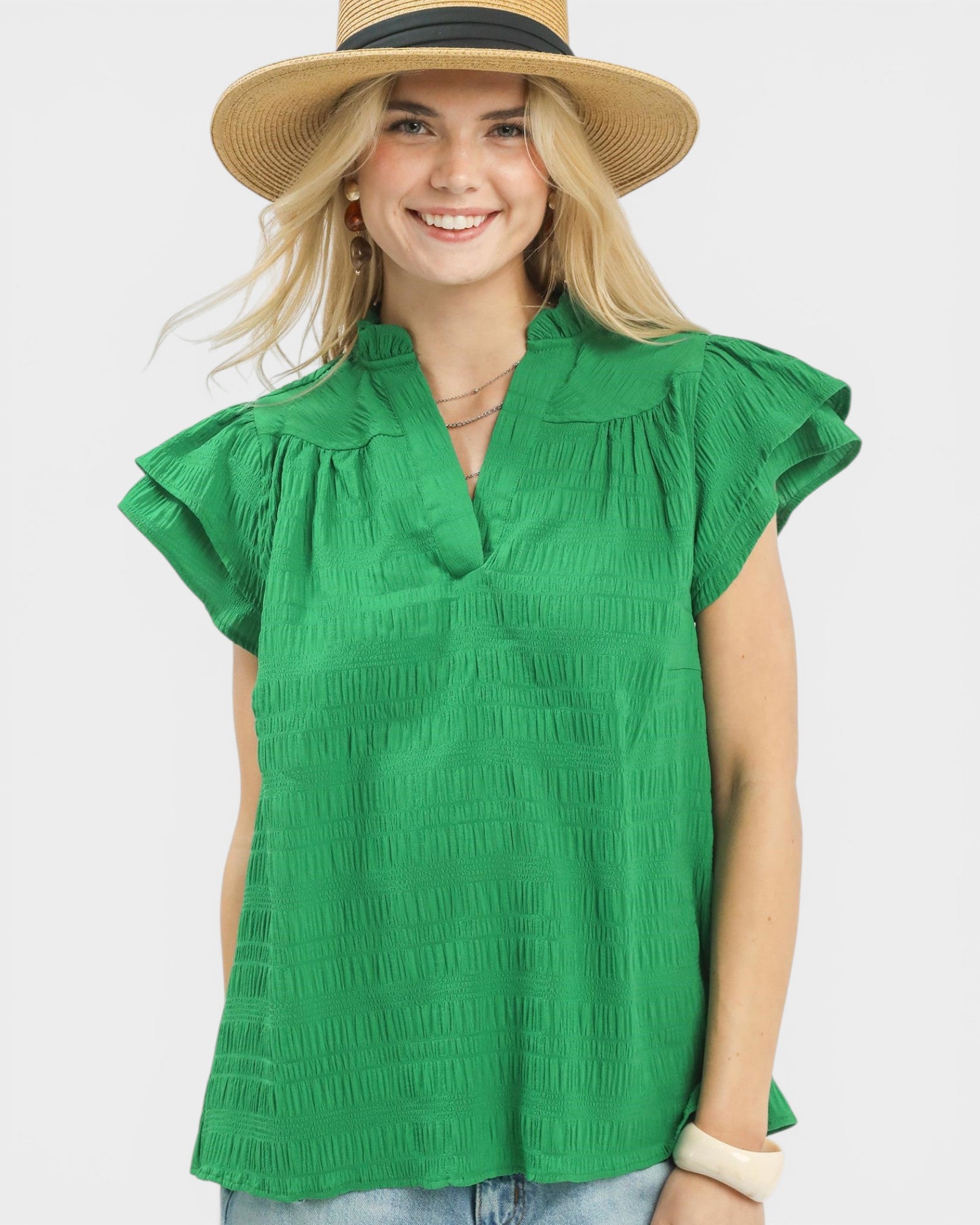 Woman wearing a green blouse with ruffled sleeves and a straw hat on a white background