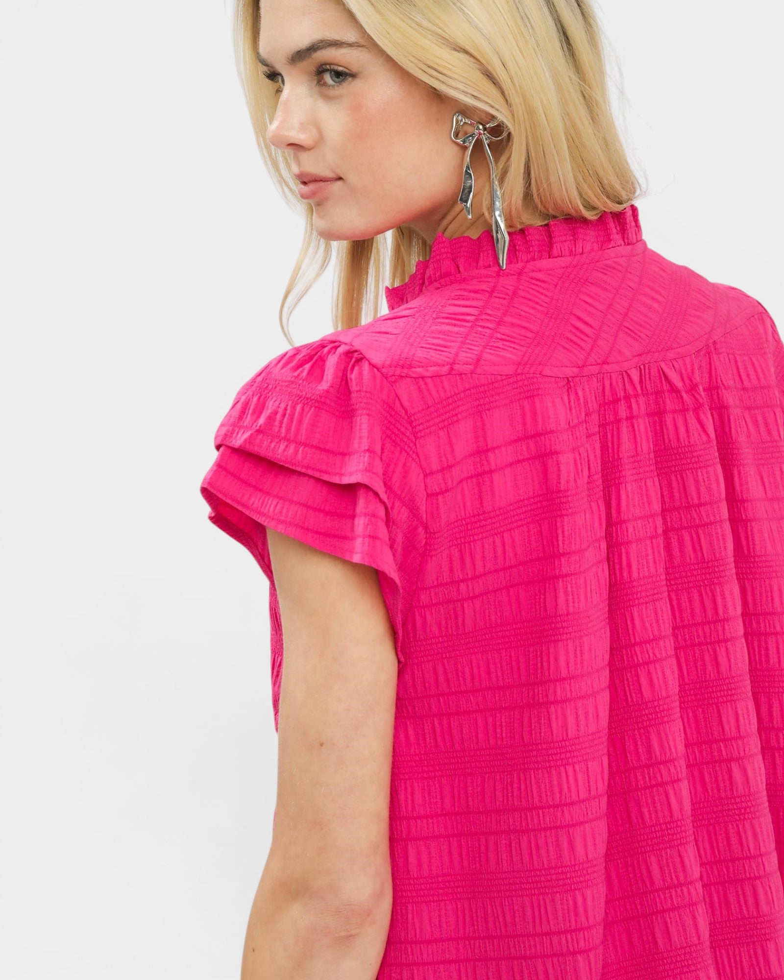 Woman wearing a bright pink textured top against a plain background