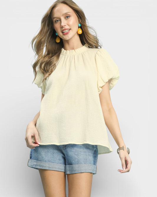 Woman wearing a light yellow blouse and denim shorts on a white background