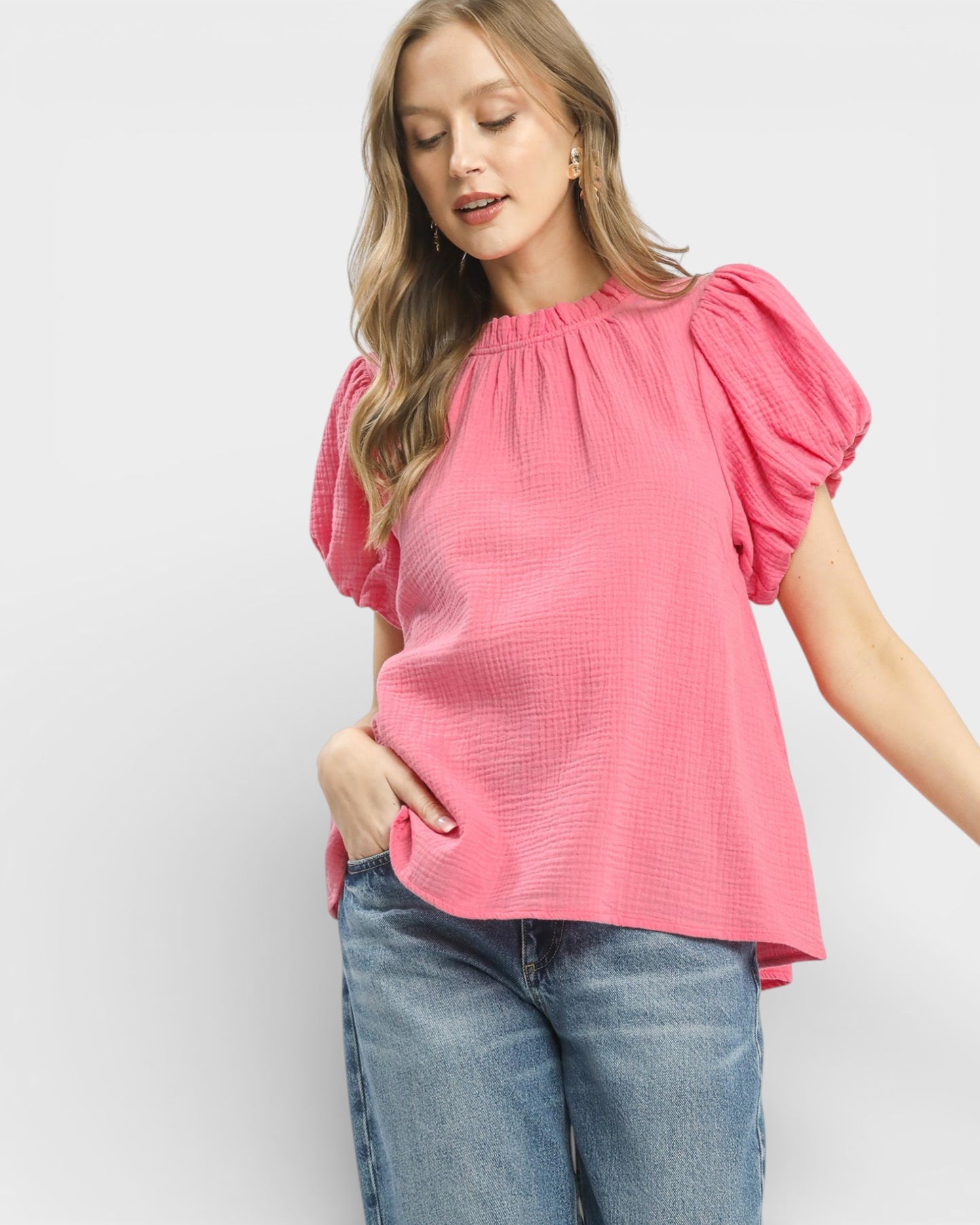 Woman wearing a pink blouse with ruffled sleeves and blue jeans on a white background