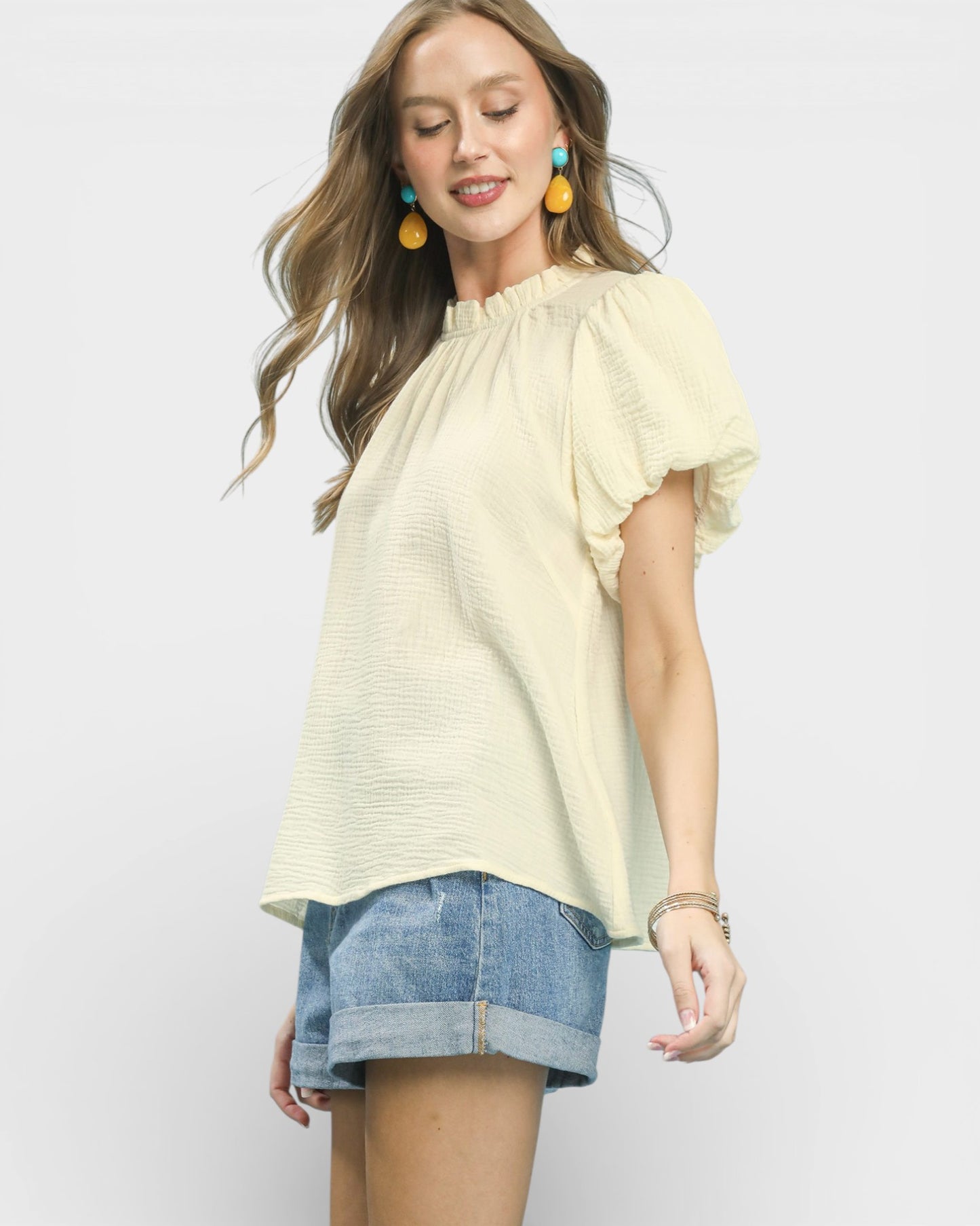 Woman wearing a light yellow blouse and denim shorts on a white background