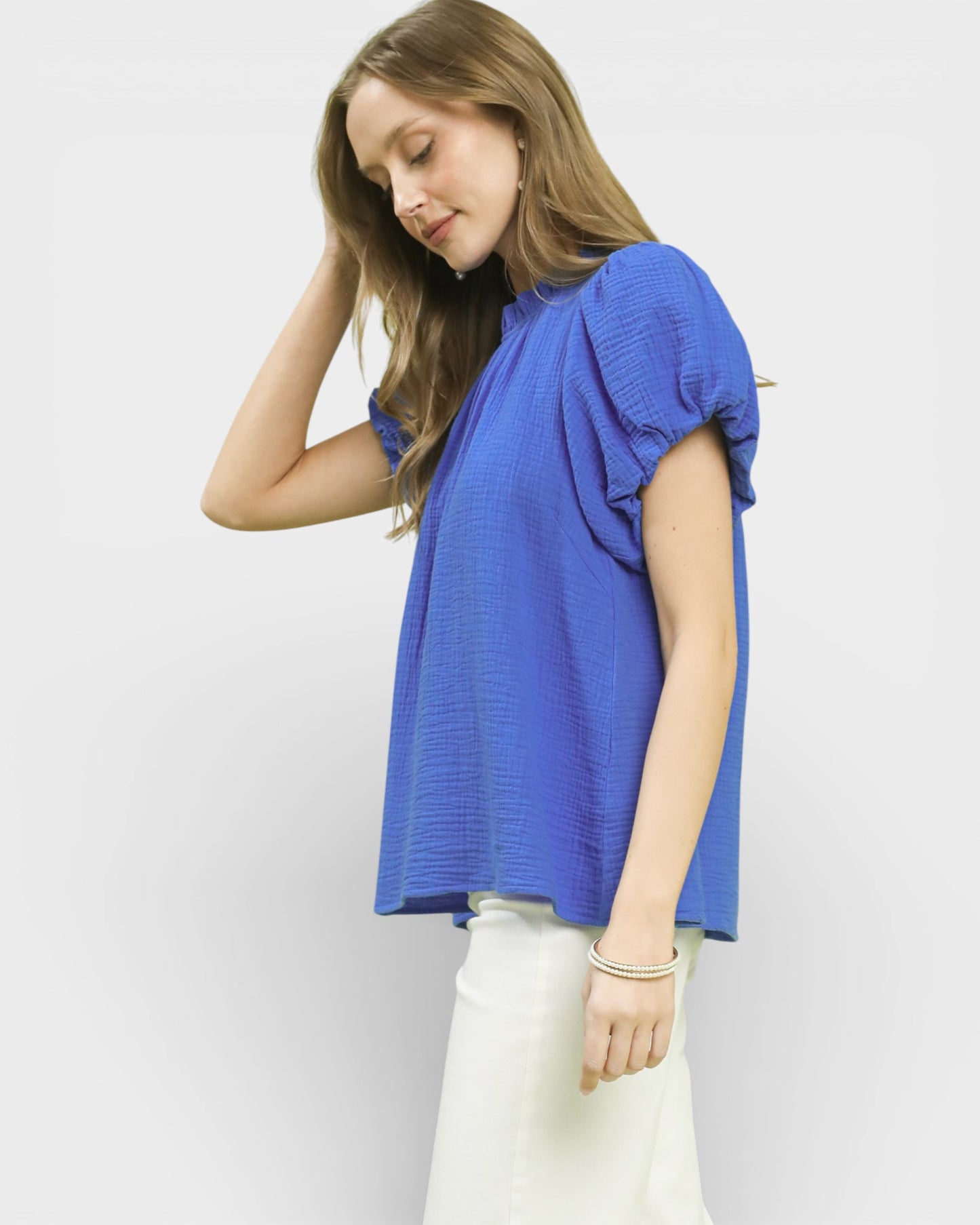 Woman wearing a blue top and white pants against a plain background