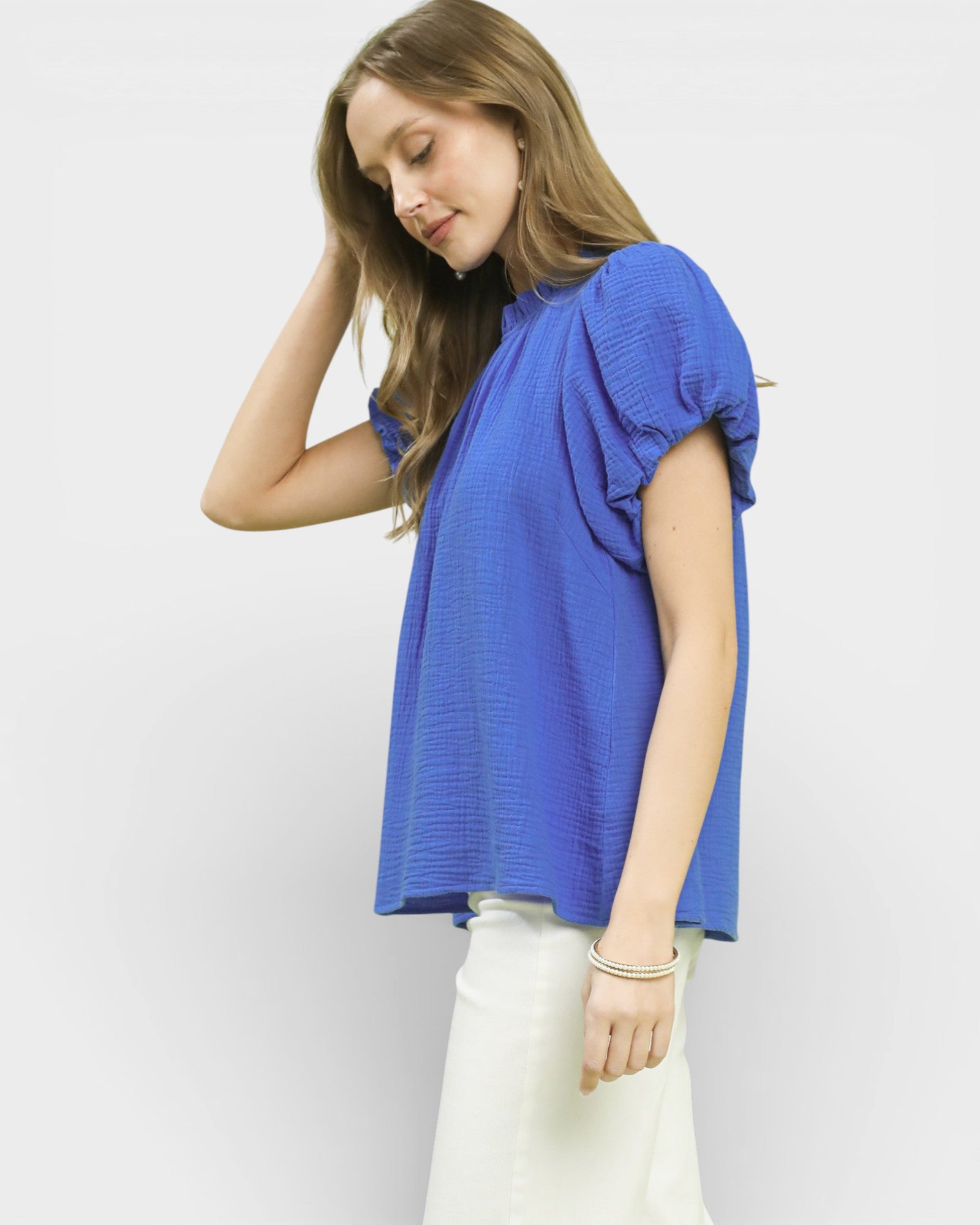 Woman wearing a blue top and white pants against a plain background